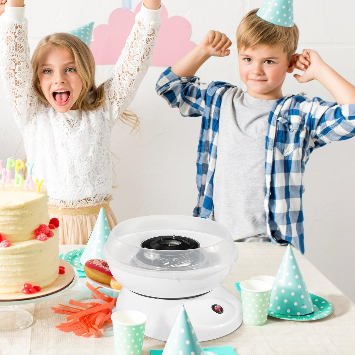 Kinder auf einer Geburtstagsfeier, ein Mädchen jubelt, ein Junge posiert. Zuckerwattemaschine und Kuchen.