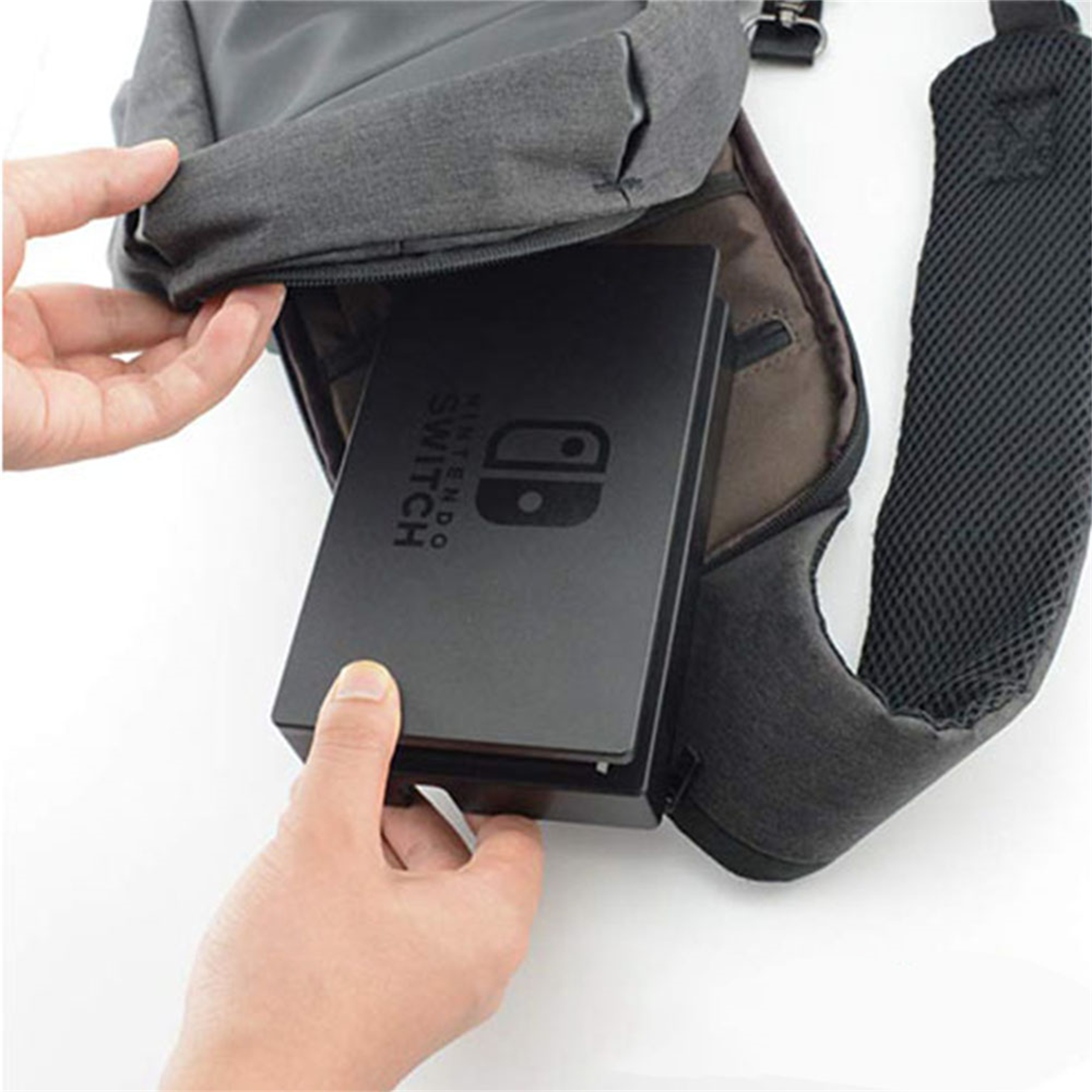 Hand hält eine Nintendo Switch-Konsole und steckt sie in eine graue Umhängetasche. Weißer Hintergrund.