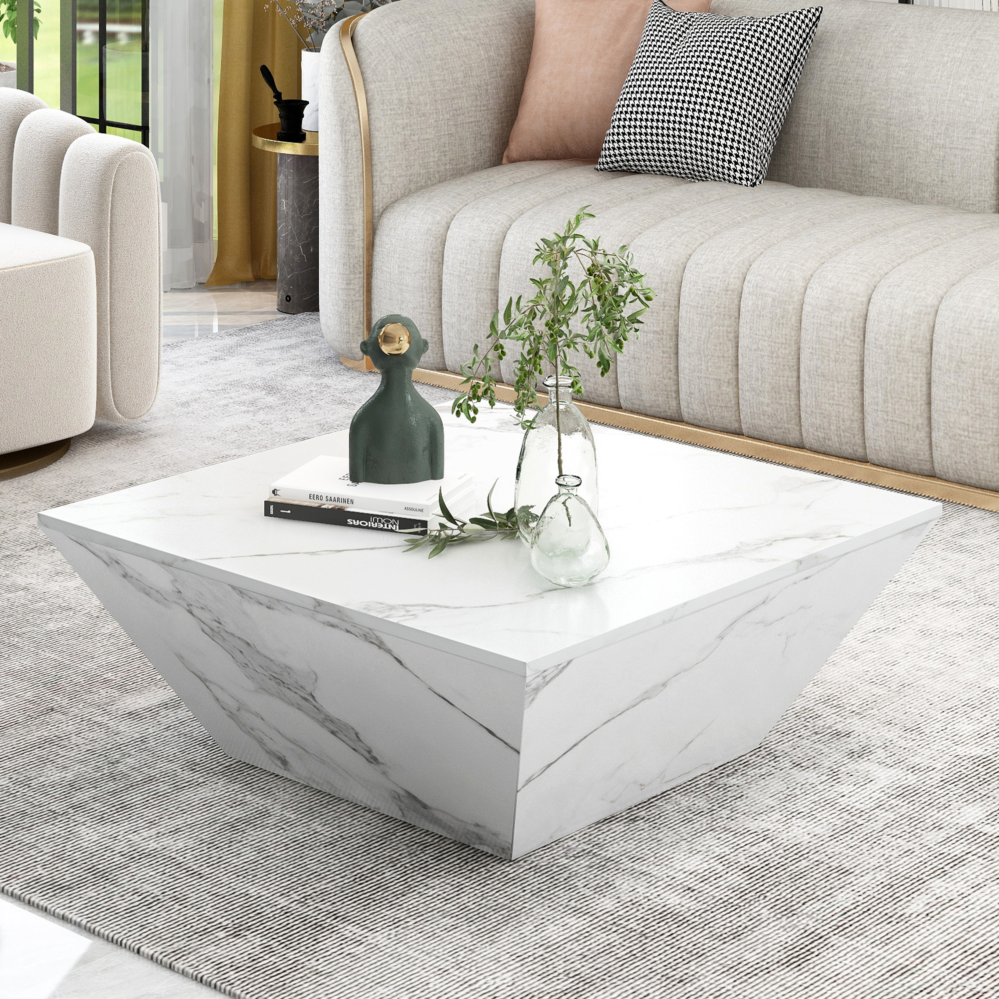 Ein weißer quadratischer Couchtisch aus Marmor mit einer Vase, einem Buch und einer grünen Skulptur.