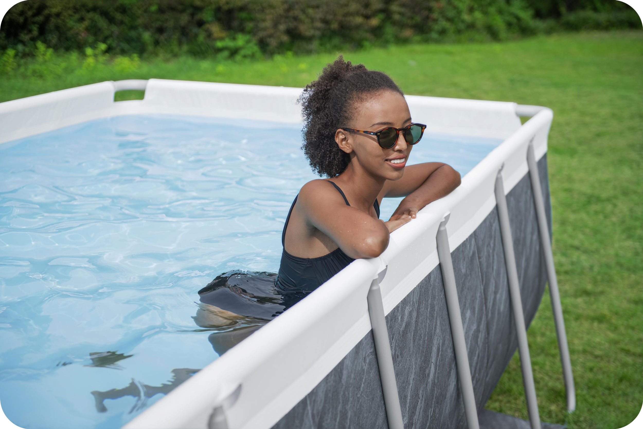 Kobieta w okularach przeciwsłonecznych w basenie, ciesząca się wodą i patrząca na bok, z zieloną trawą dookoła.