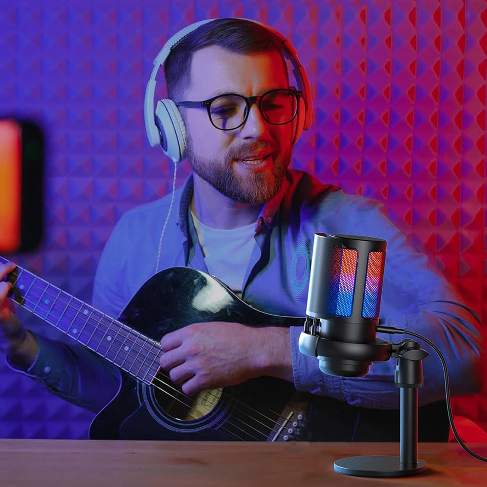 Ein Mann mit Brille und Kopfhörern spielt Gitarre und singt in ein schwarzes Mikrofon mit RGB-Lichtern.