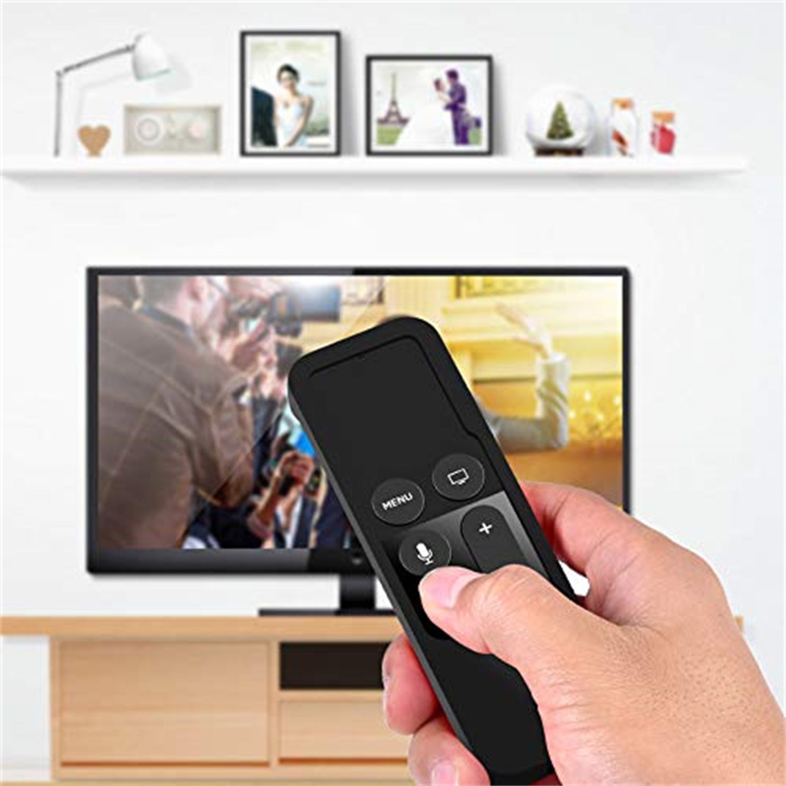 Hand hält eine schwarze Fernbedienung, Fernseher im Hintergrund.