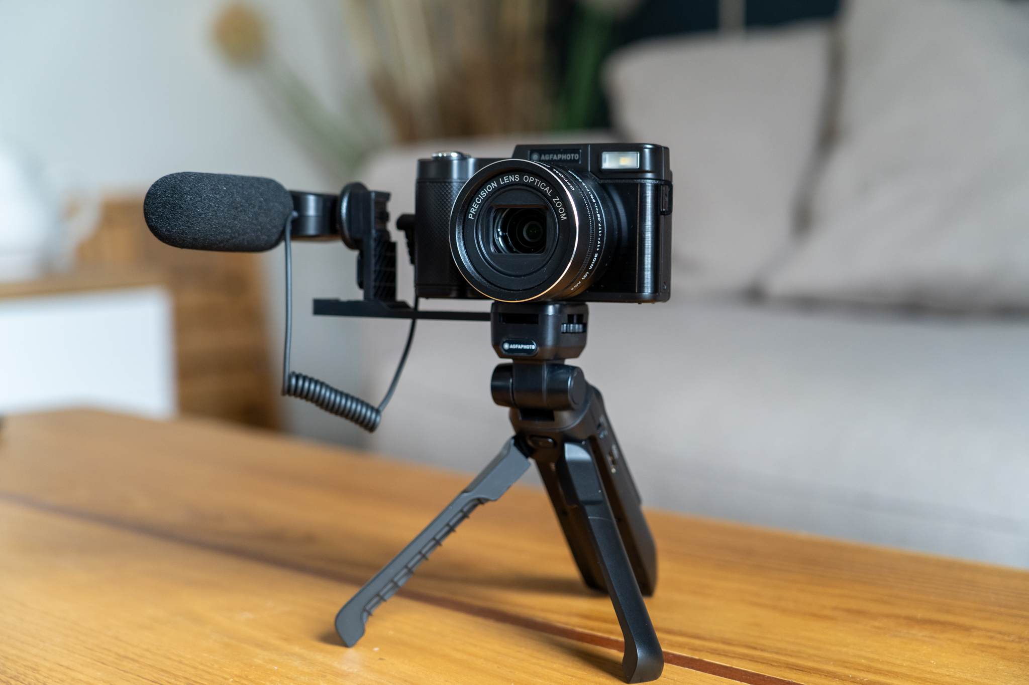 Czarny aparat z mikrofonem na statywie, drewniany stół z kanapą w tle.