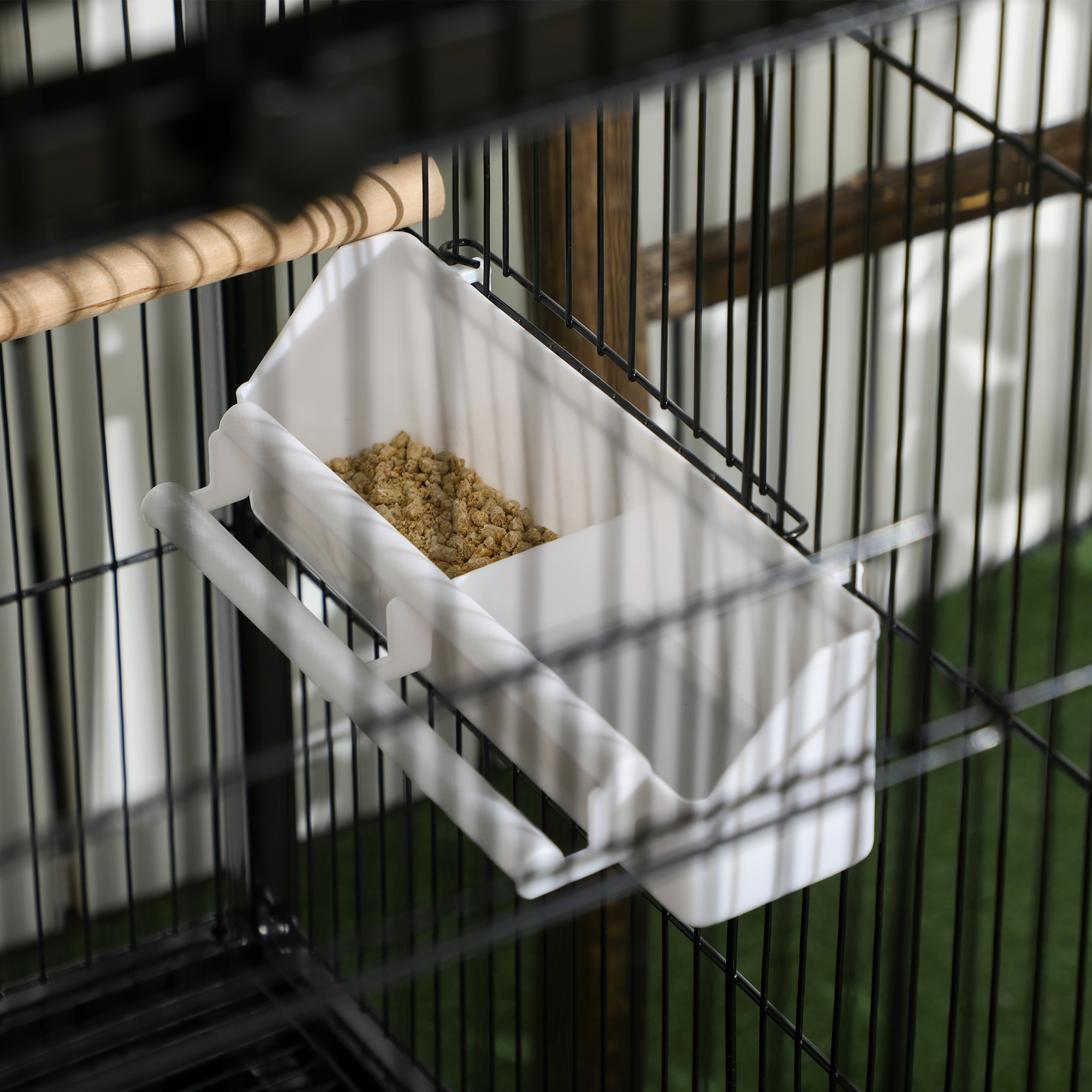Primer plano de un comedero blanco para pájaros dentro de una jaula negra con comida.