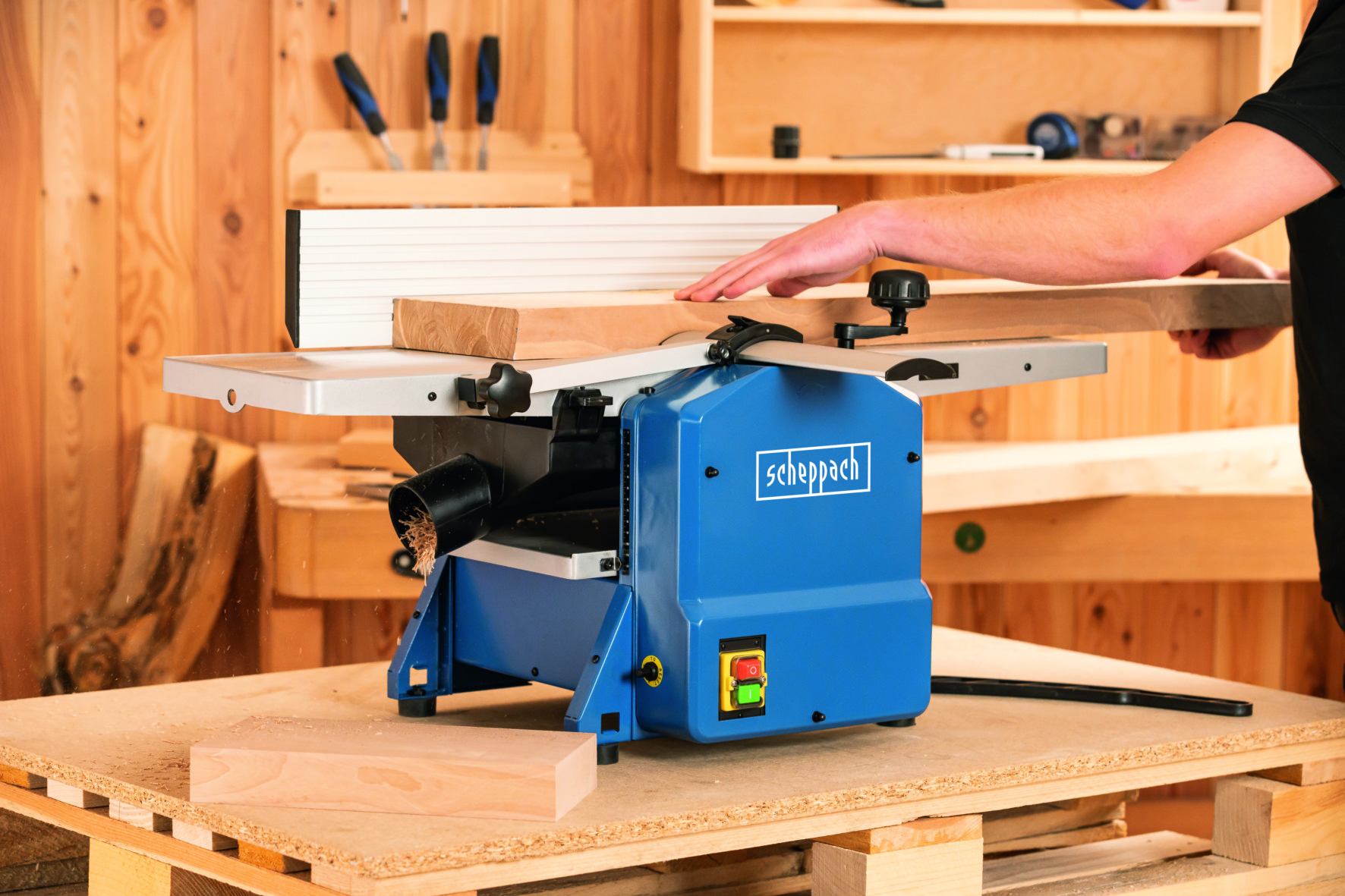 Eine blaue und graue Hobelmaschine auf einer Holzoberfläche, in die eine Person ein Stück Holz einführt.