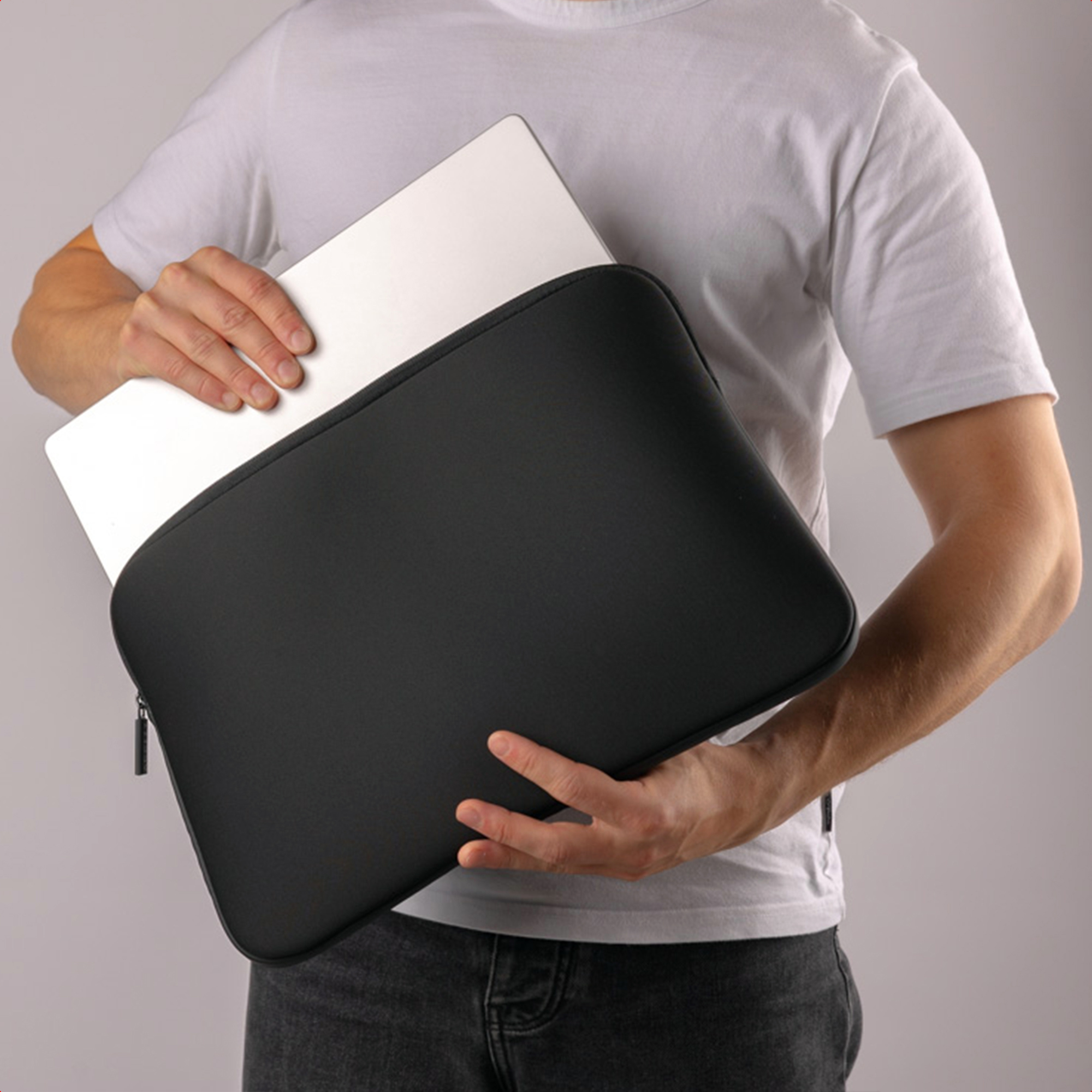 A person holding a black laptop sleeve with a laptop inside. The sleeve is black and the background is gray.