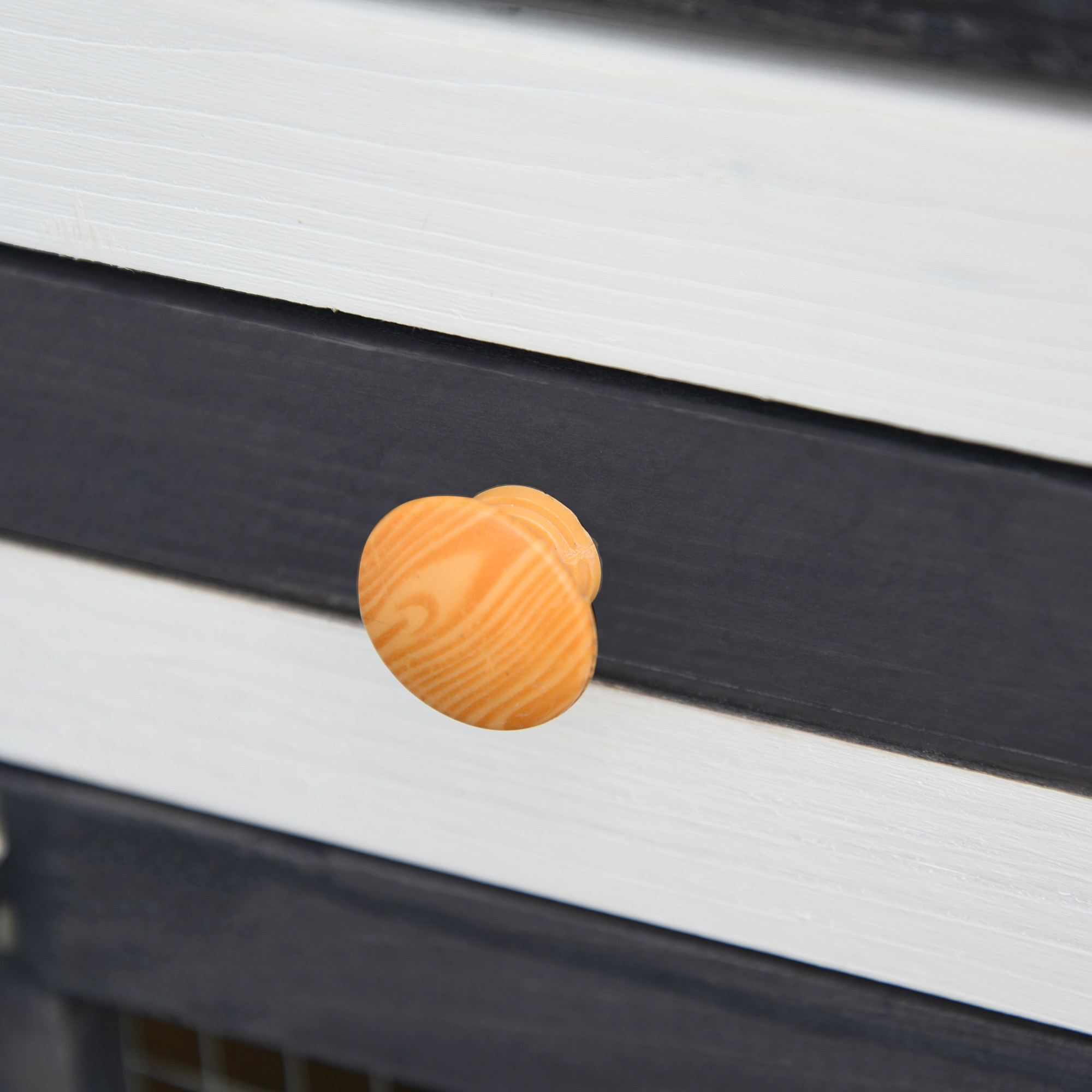 Primer plano de una perilla de madera en una puerta de armario de dos tonos. La perilla es naranja y veteada.