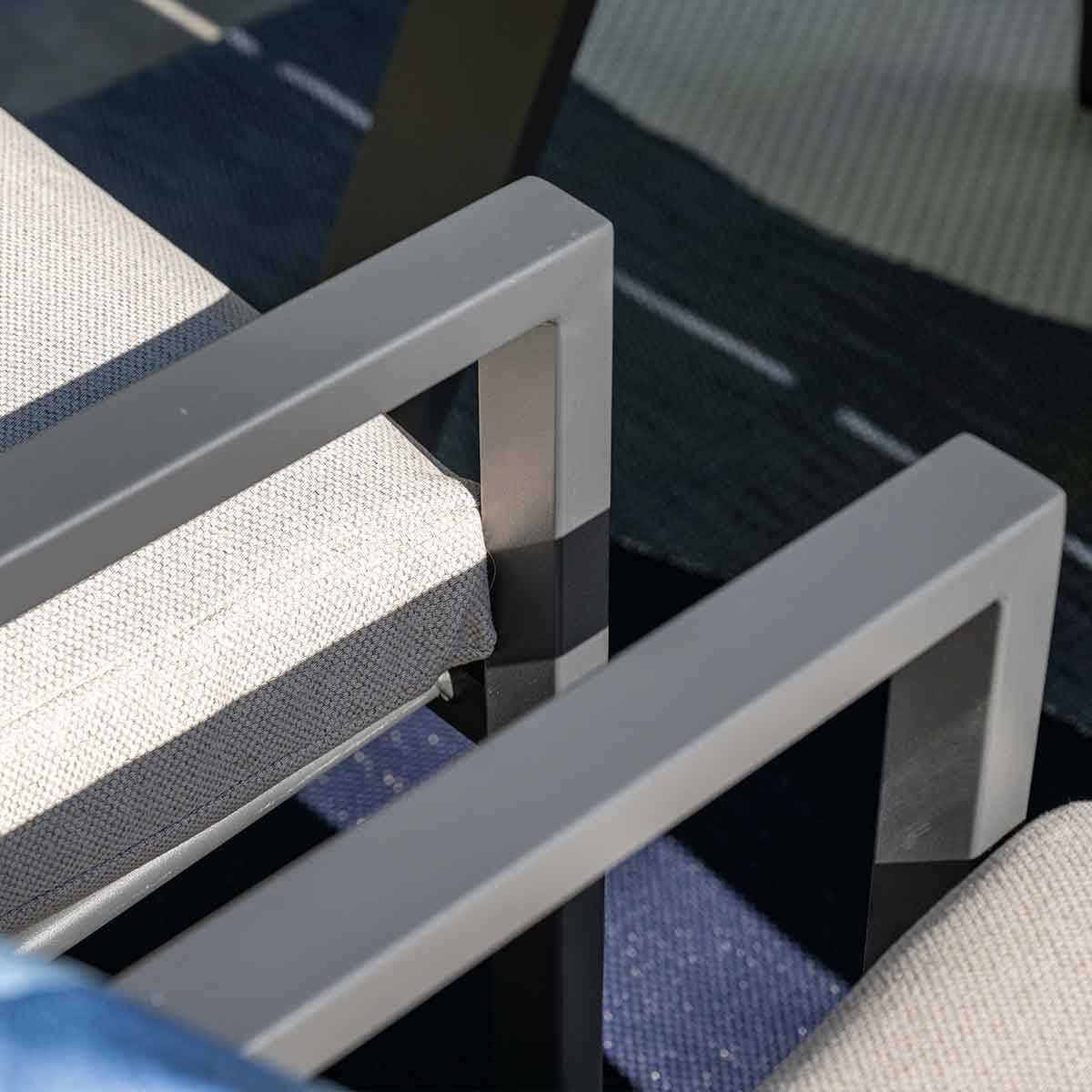 Close-up van grijze metalen armleuningen van een stoel, op een blauw en wit patroonkleed, met een vage achtergrond.