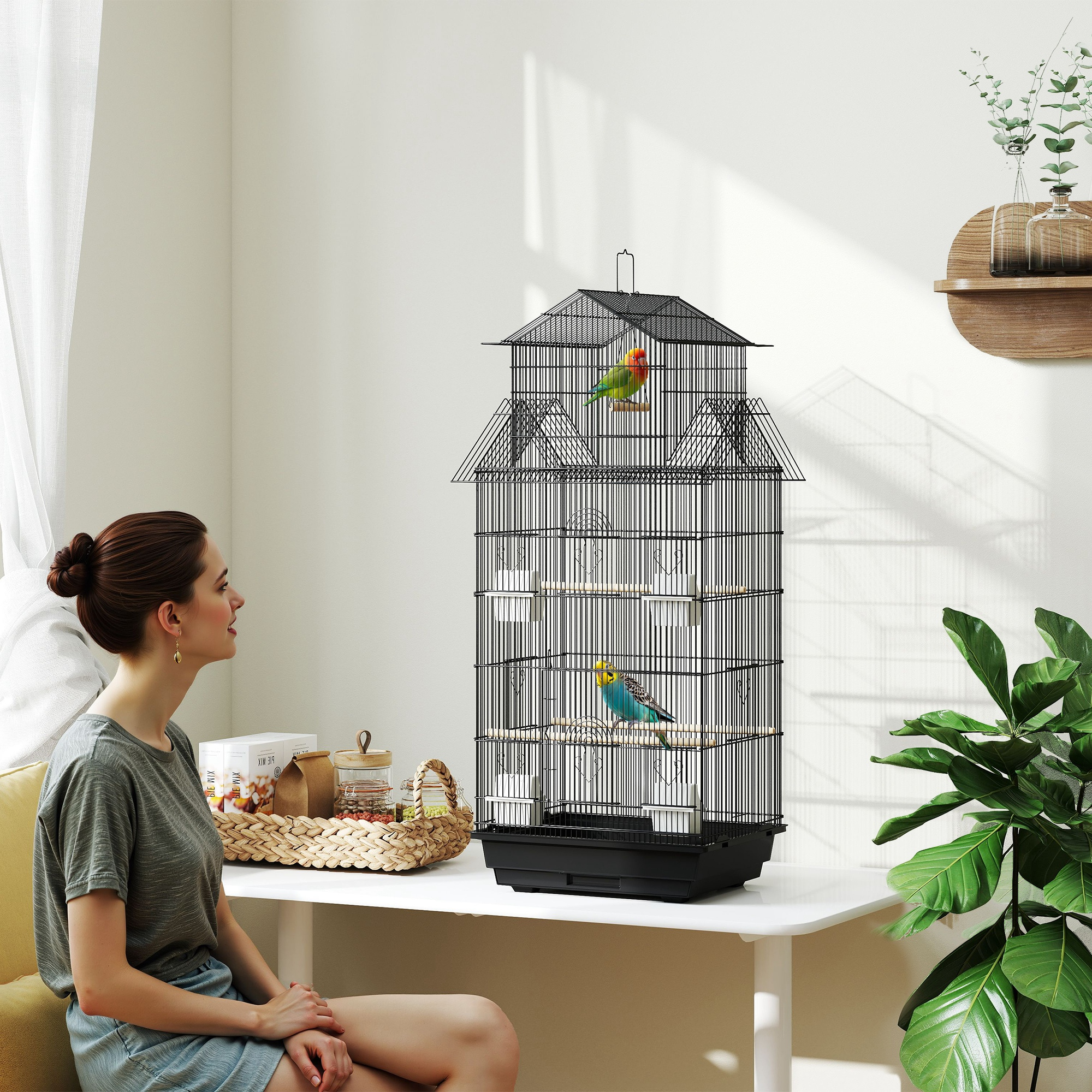Una mujer sentada cerca de una jaula con dos pájaros. La jaula está sobre una mesa.