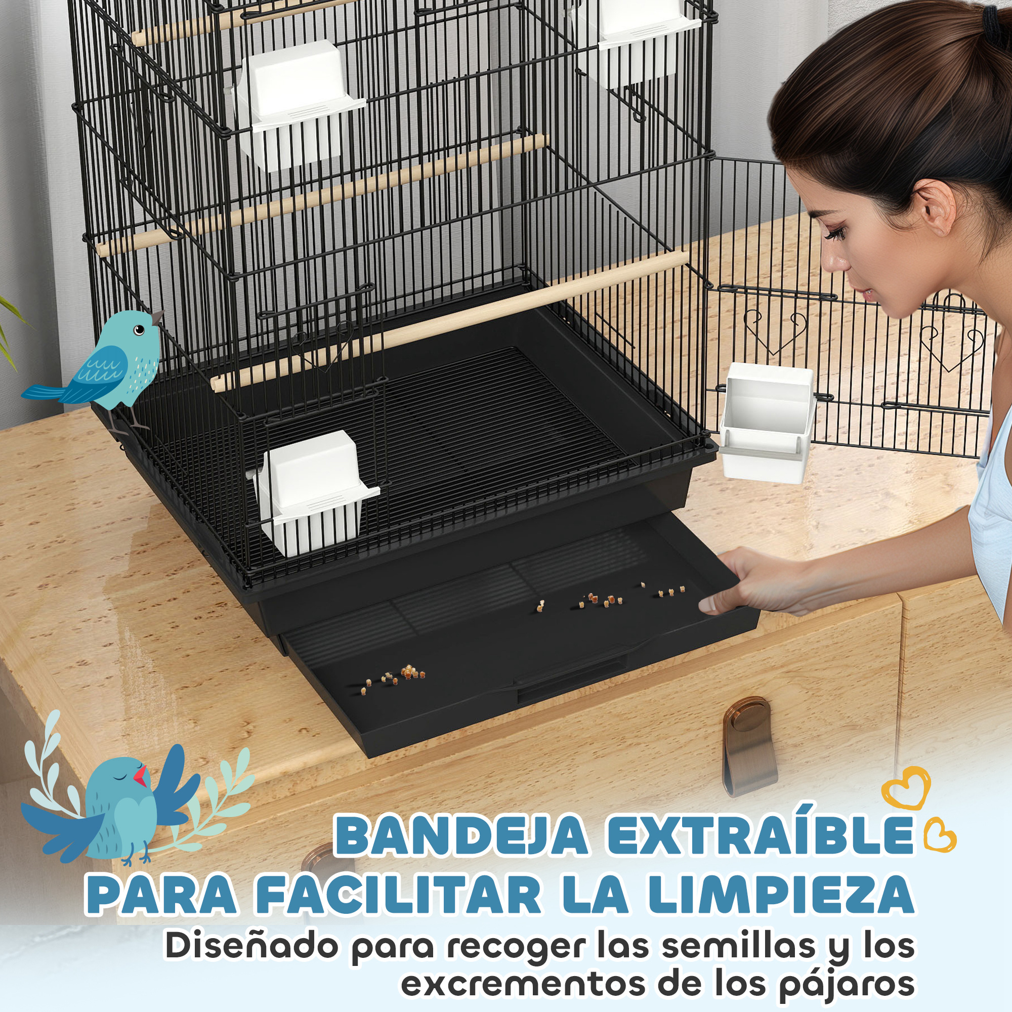 Una jaula para pájaros negra con una bandeja extraíble y una mujer limpiándola sobre una mesa de madera.