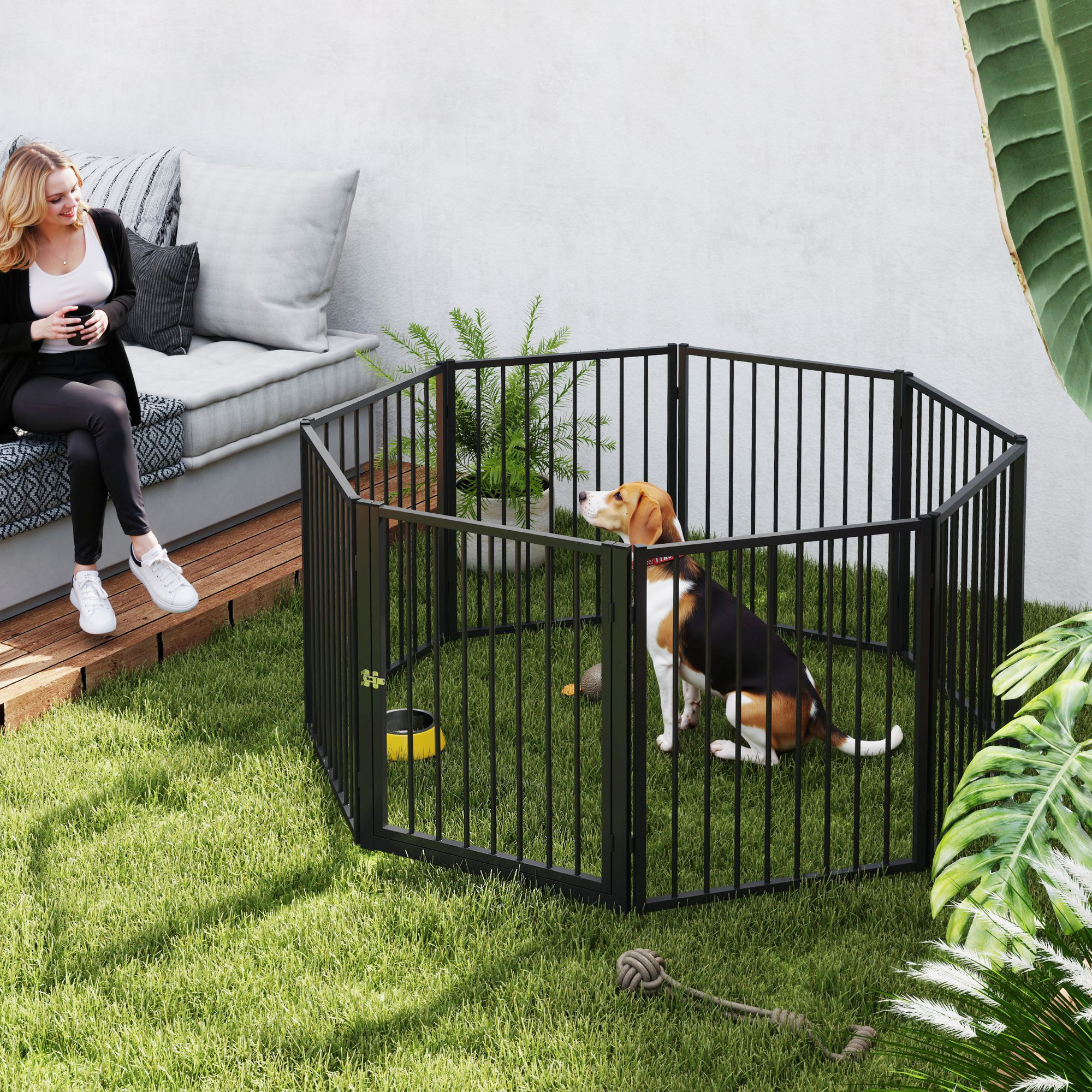Un parque para perros de metal negro en un área cubierta de hierba con una mujer y un perro.