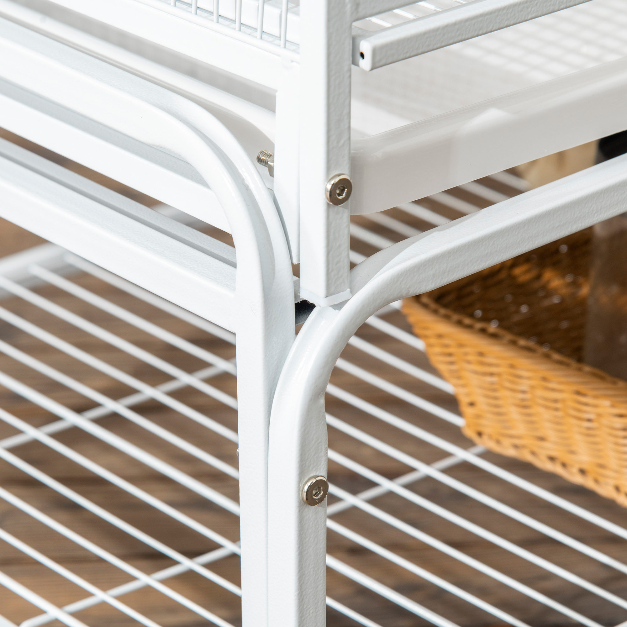Primer plano de una estantería de metal blanco con una cesta de mimbre visible debajo, sobre un suelo de madera.