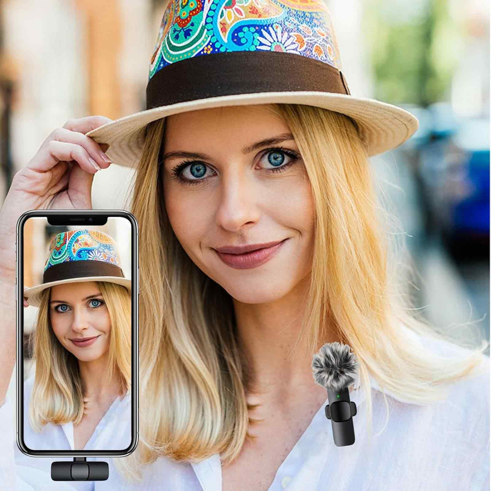 Eine Frau mit Hut lächelt. Ein Telefon zeigt ein Selfie. Ein Mikrofon ist an ihrem Hemd.