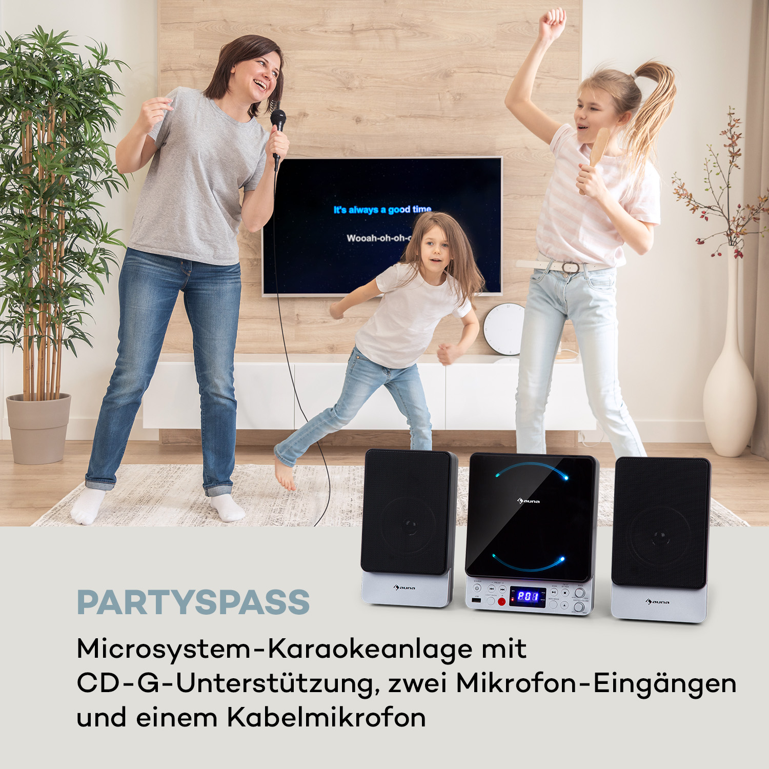 Drei Personen singen Karaoke. Zwei Lautsprecher stehen vor dem Fernseher. Auf den Lautsprechern leuchten Lichter.