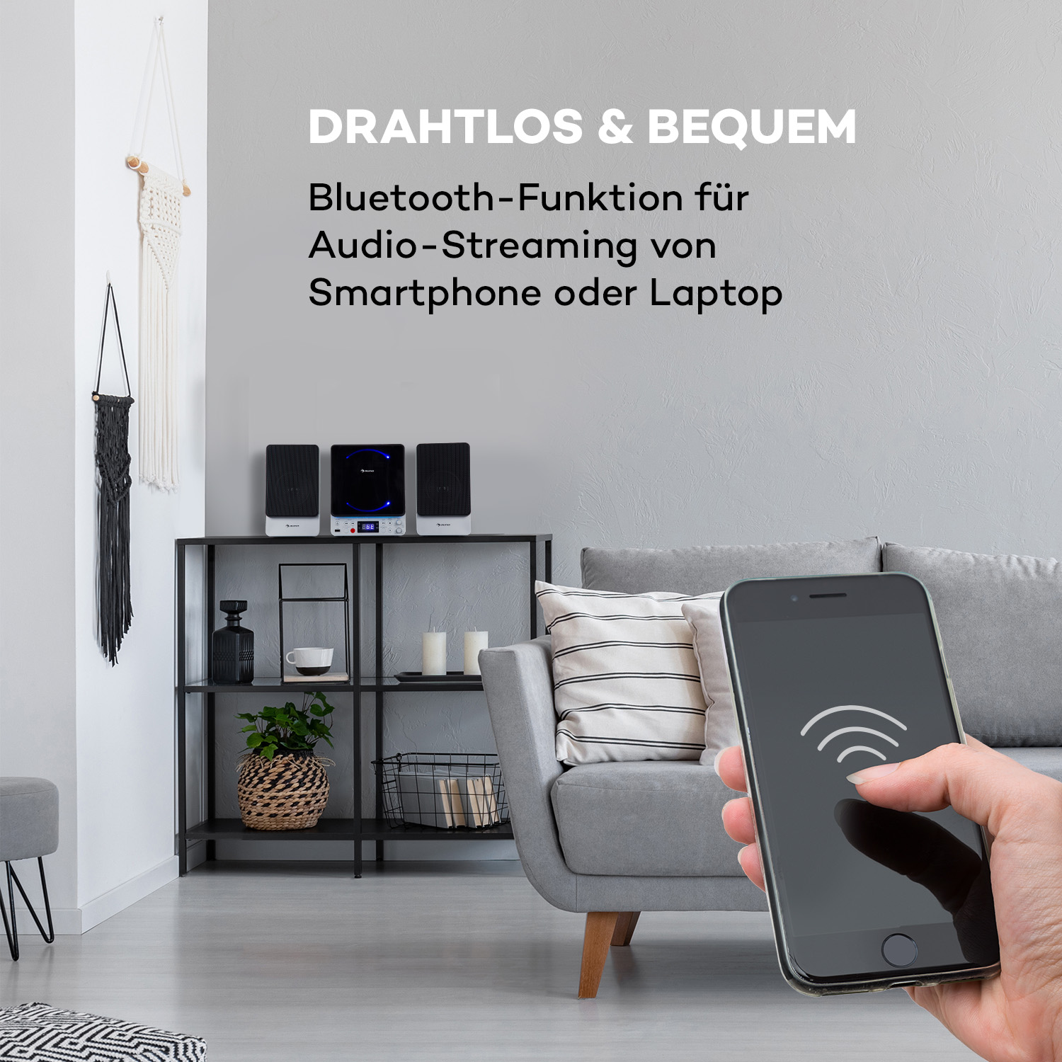 Eine Person, die ein Telefon mit einem WLAN-Signal auf dem Bildschirm, einer Couch und zwei Lautsprechern hält.