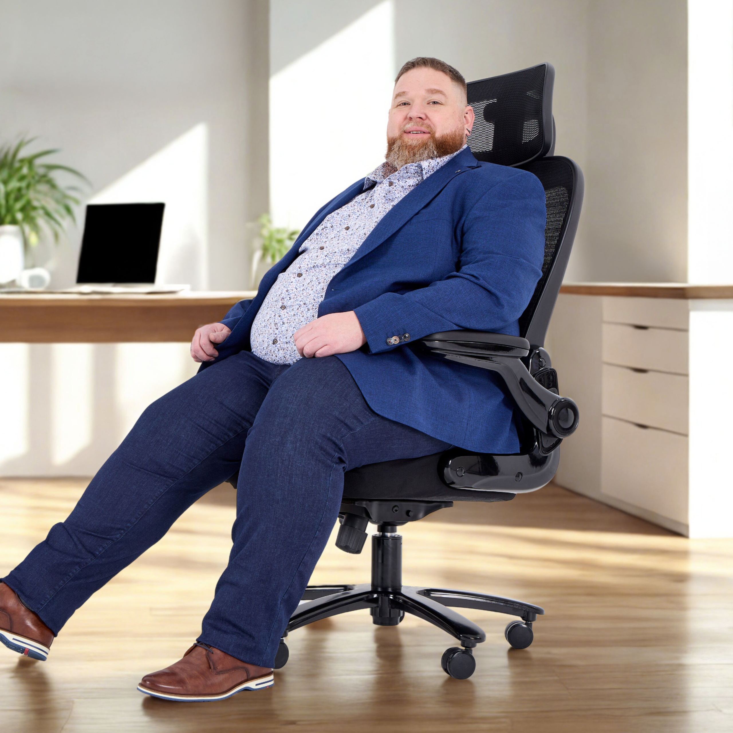 Ein Mann in einer blauen Jacke sitzt in einem schwarzen Bürostuhl und lächelt in die Kamera. Ein Schreibtisch ist dahinter.
