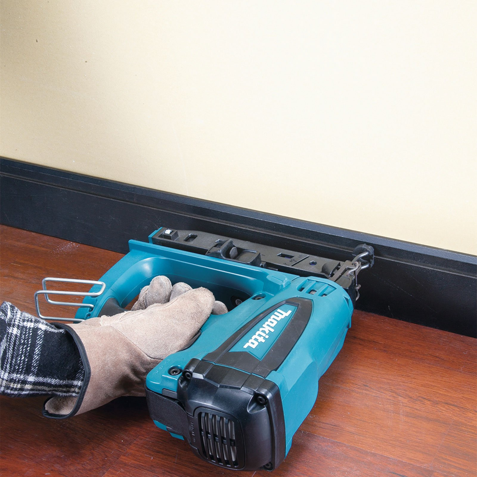 Una persona usa una sparachiodi su un telaio in legno. L'utensile è verde acqua e nero. Il telaio è nero e il muro beige.