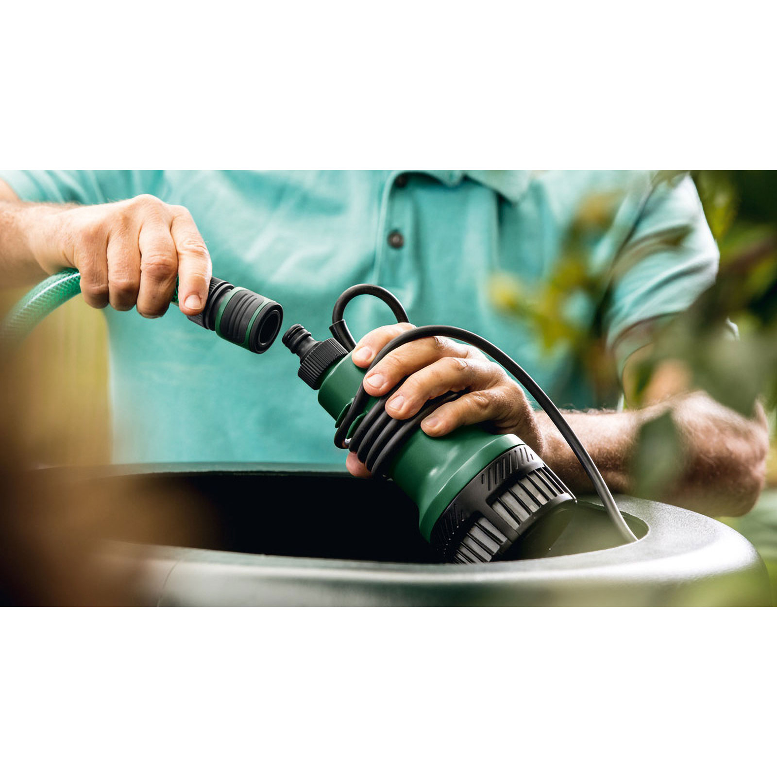 Eine Person verbindet einen grünen Schlauch mit einer grünen Pumpe. Sie stehen über einem dunkelgrünen Behälter.