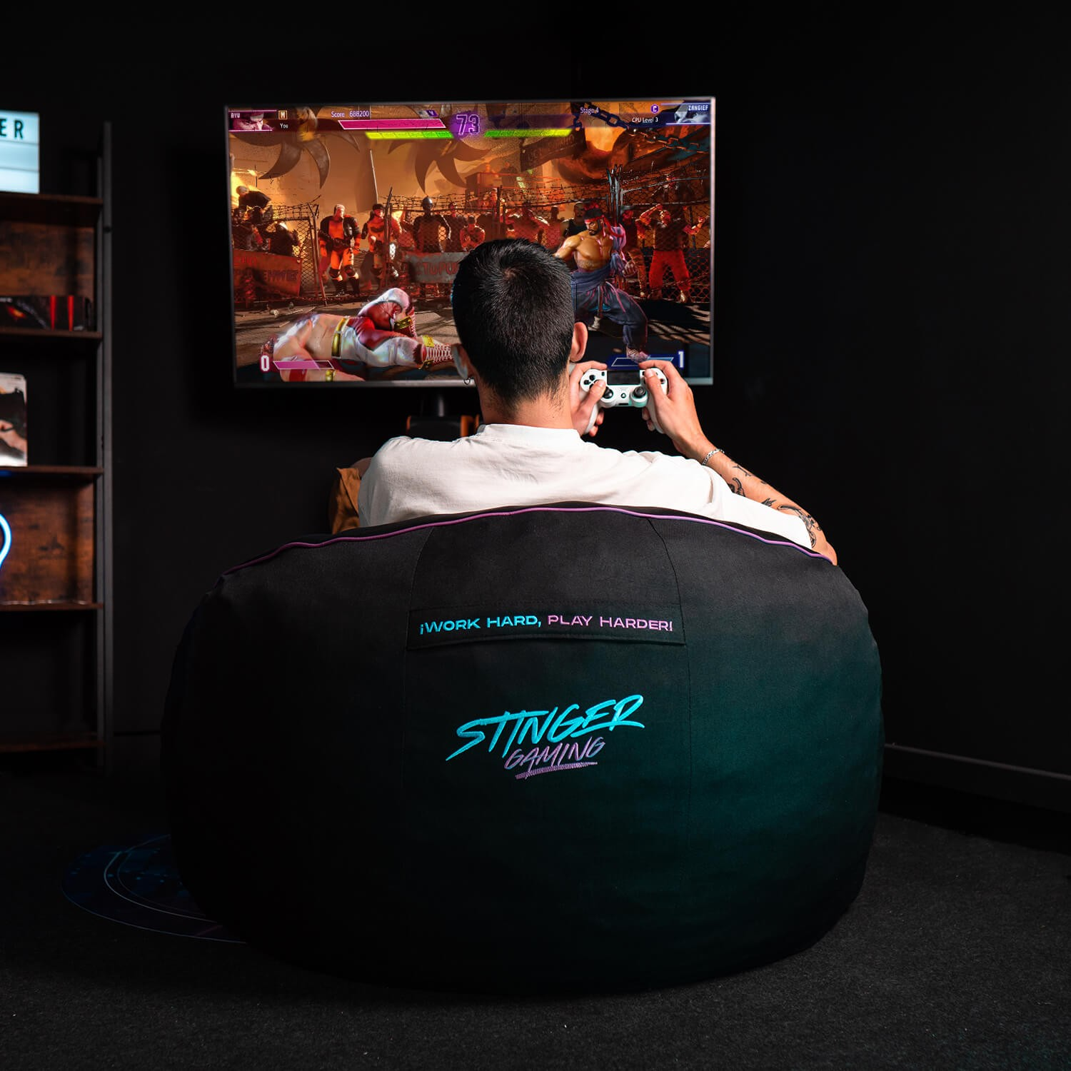 Persona jugando en TV. Silla de saco con texto 'STINGER GAMING'. Habitación oscura. Alfombrilla gaming.