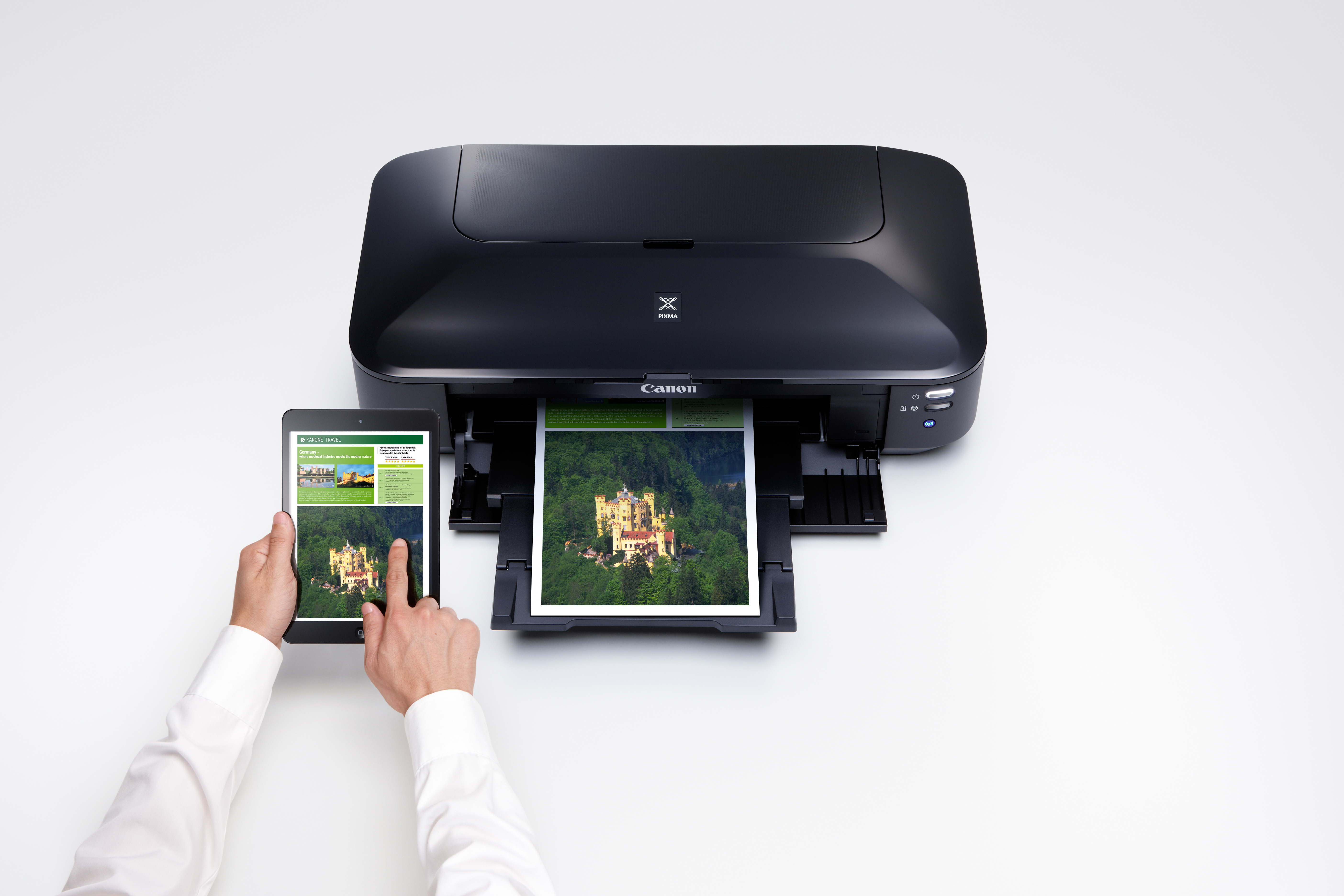 Una stampante Canon nera è collegata a un tablet che mostra un'immagine. Una stampa è nel vassoio.
