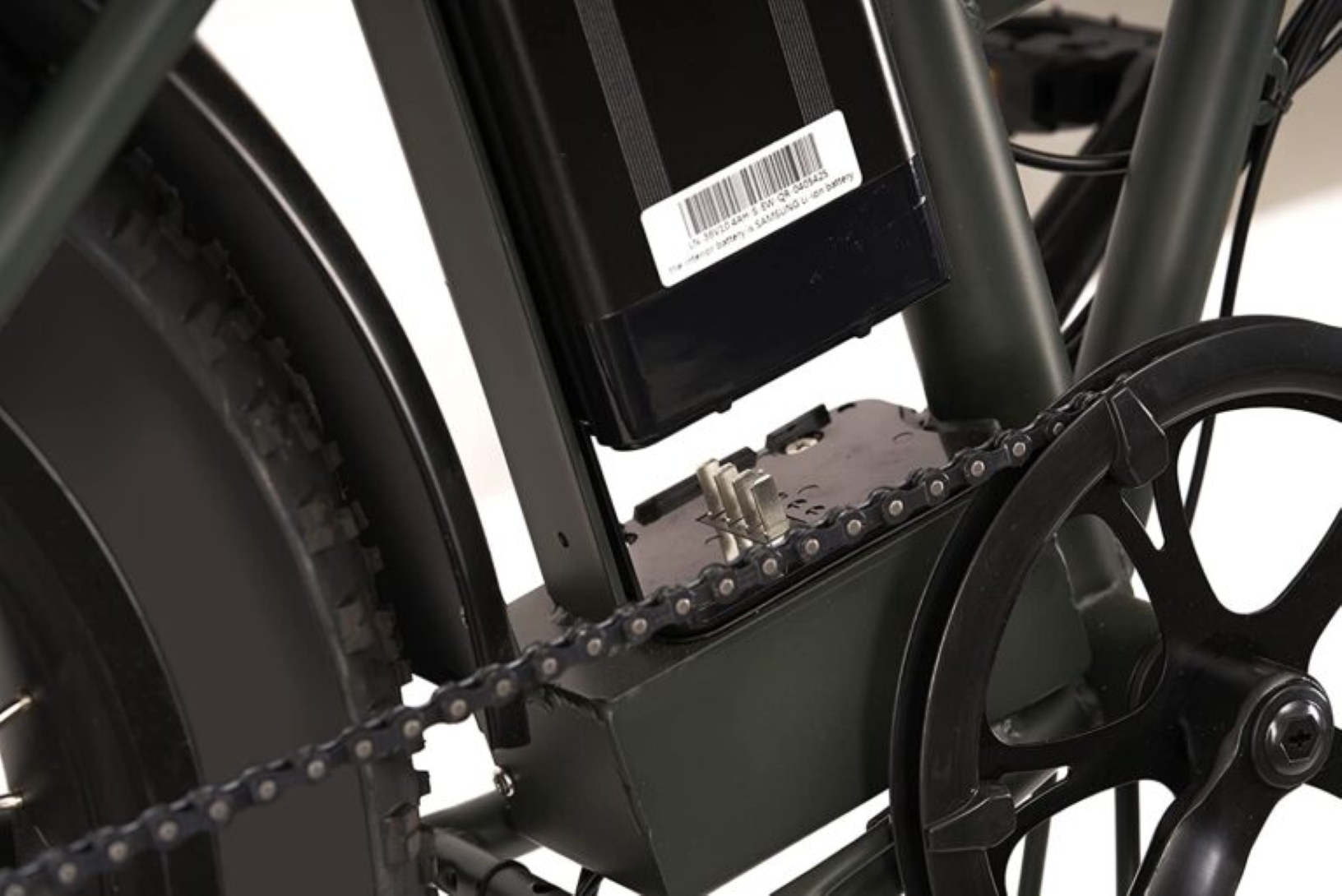 Primo piano della catena e del supporto batteria di una bici. Catena e componenti sono scuri.