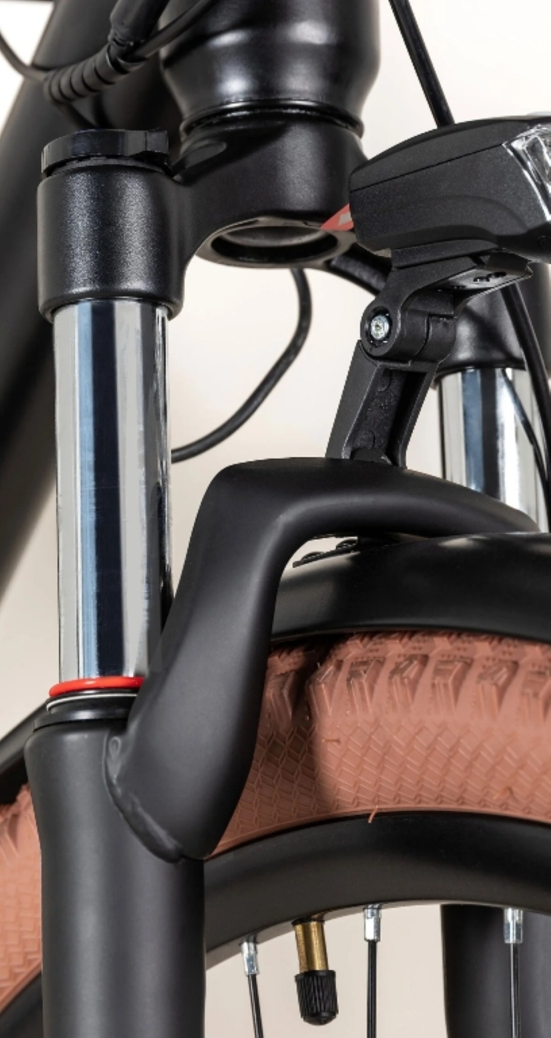 Primo piano della sezione anteriore di una bici, inclusa la sospensione anteriore, il faro e un pneumatico marrone.