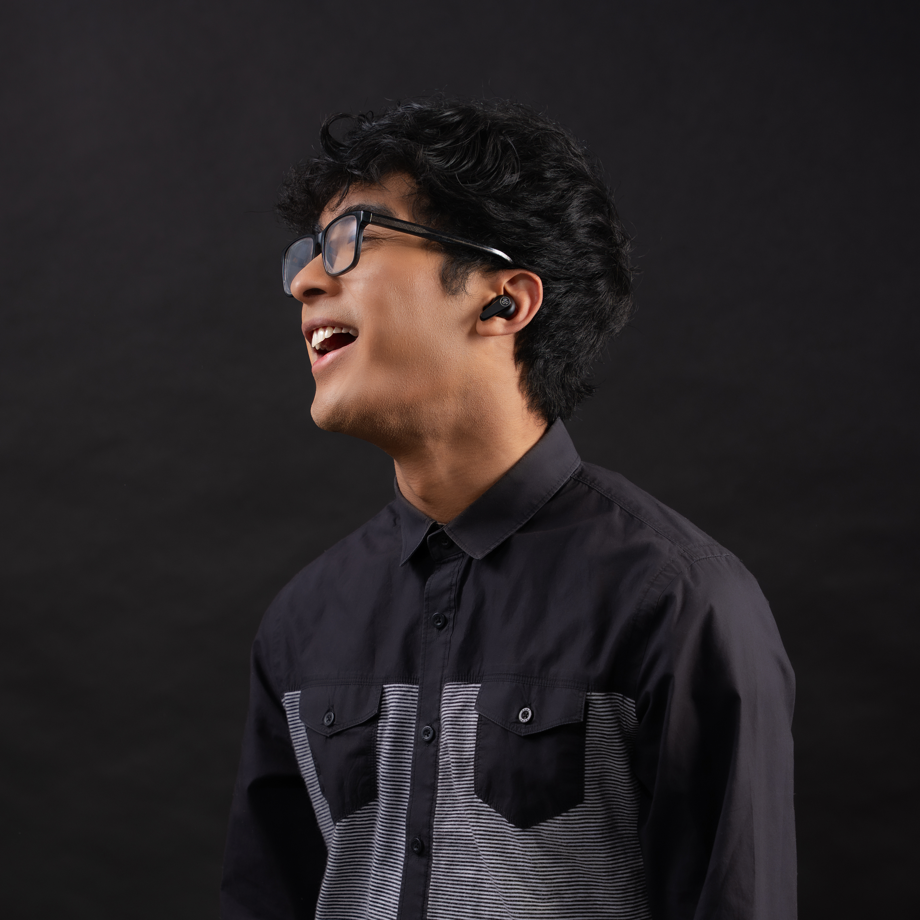 Un uomo con camicia nera e occhiali con un auricolare wireless nell'orecchio sinistro.