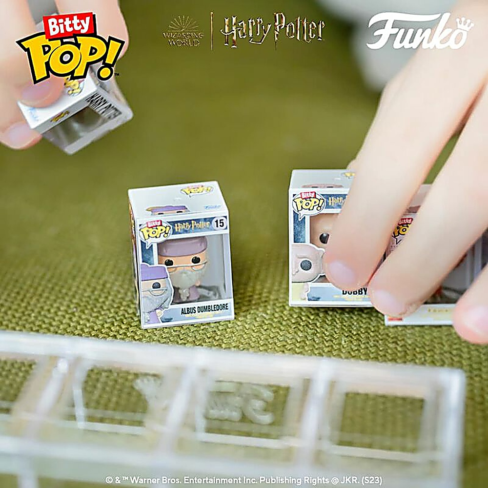 Dwie małe pudełka Funko Pop! są trzymane w dłoniach, z figurkami Harry'ego Pottera. Widać przezroczystą półkę.