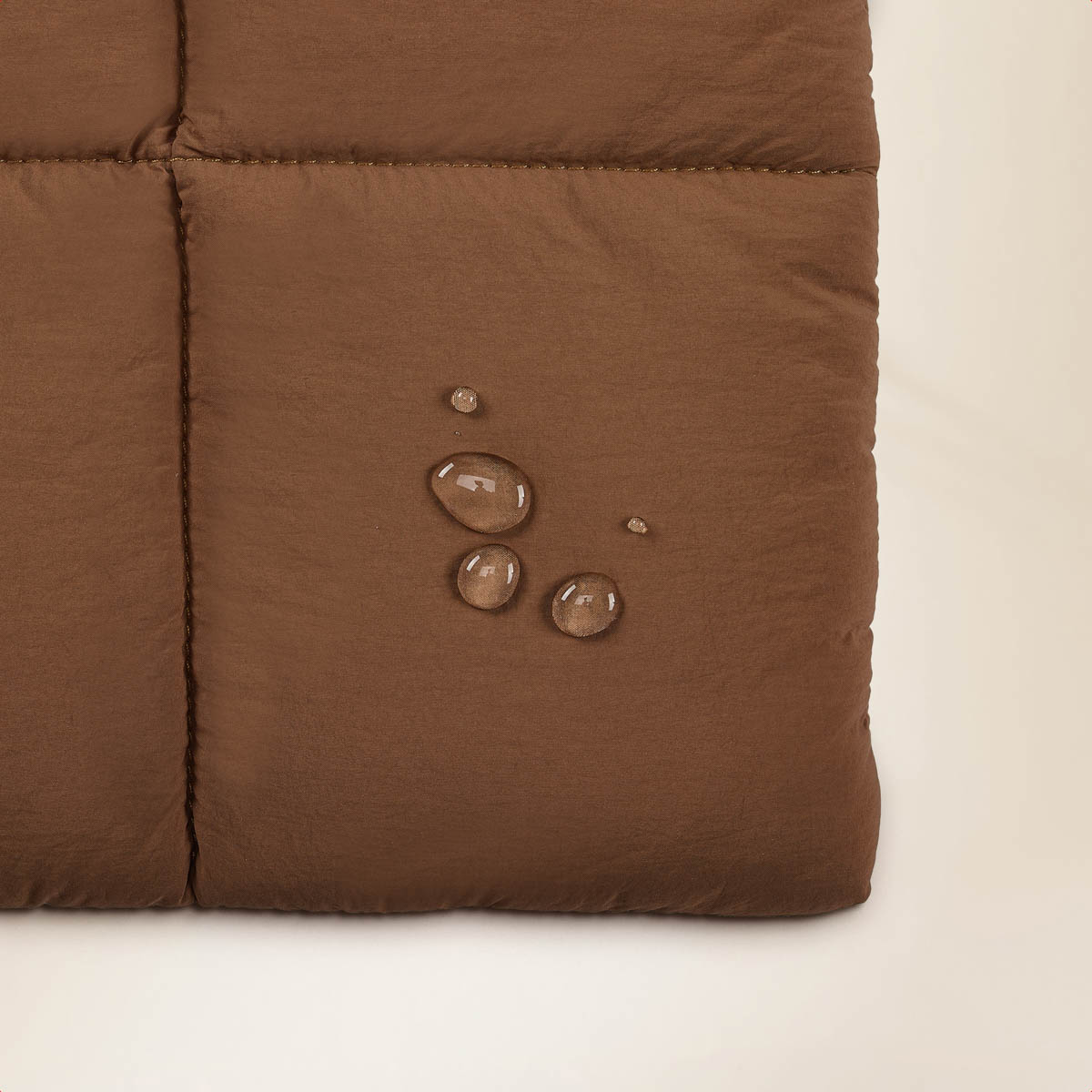 Close-up of brown quilted fabric with water droplets. Light background. Shows texture and slight sheen.