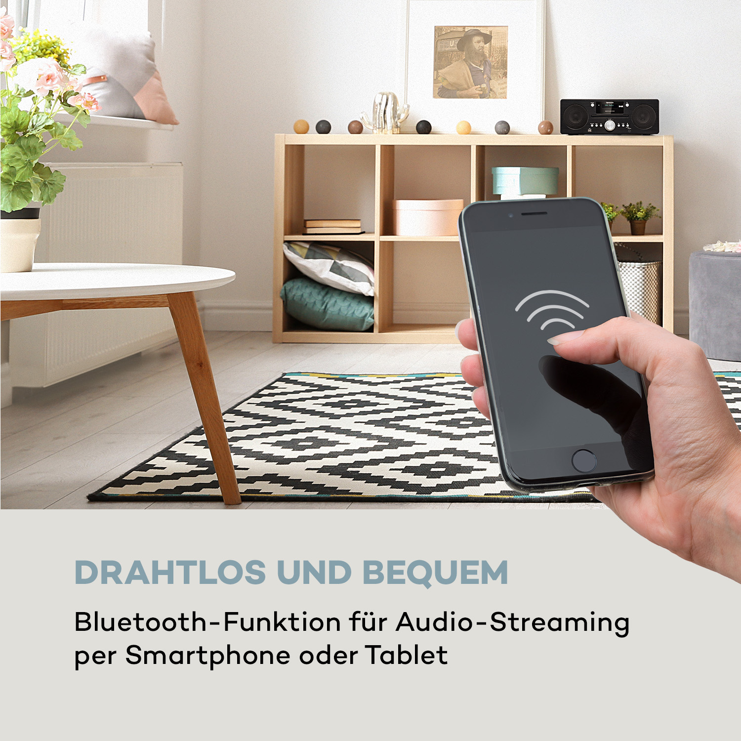 Eine Hand hält ein Smartphone mit WLAN-Symbol in der Nähe eines Radios. Ein Regal und ein Tisch sind sichtbar.