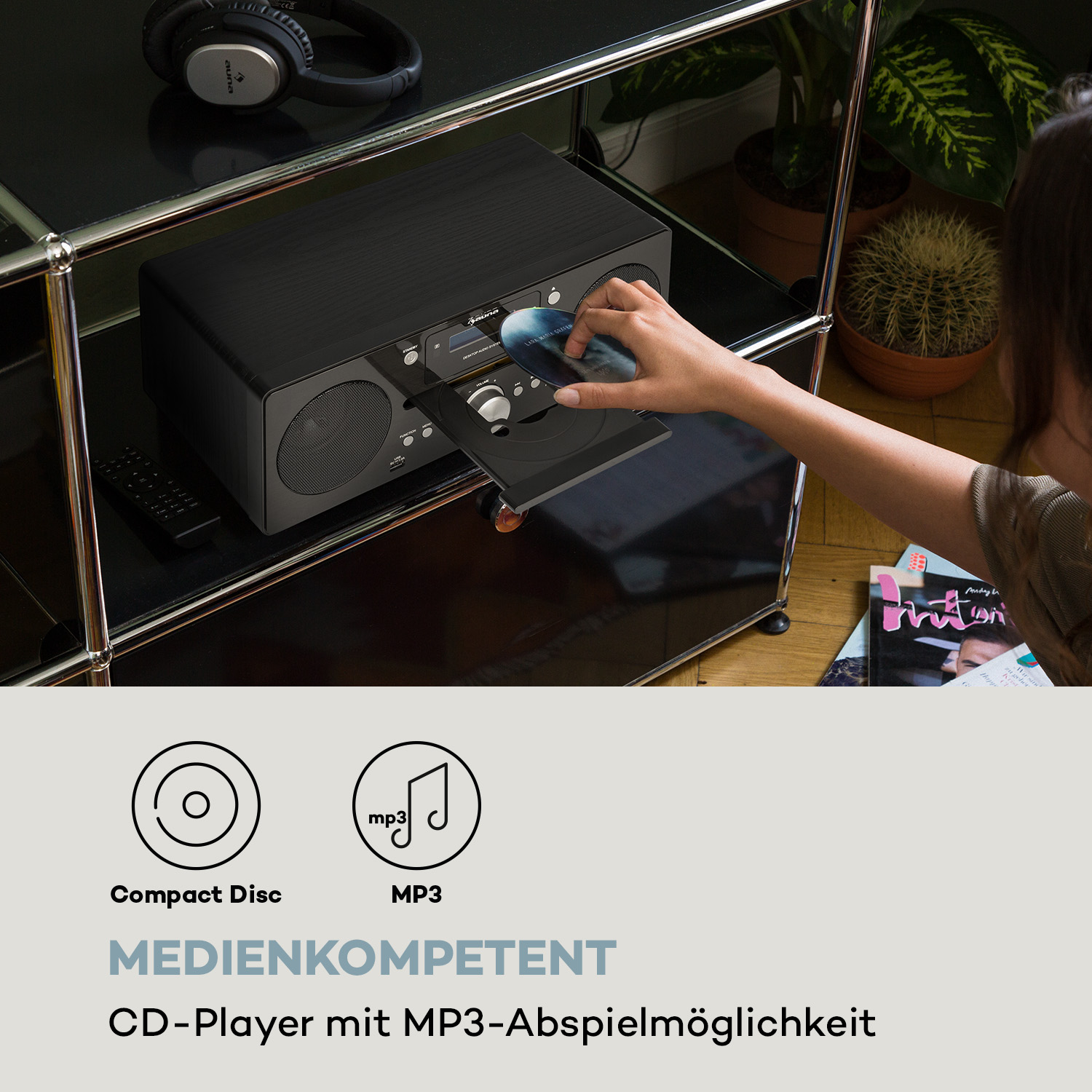 Eine Frau legt eine CD in einen schwarzen Radio-CD-Player ein. Das Radio steht auf einem schwarzen Regal.