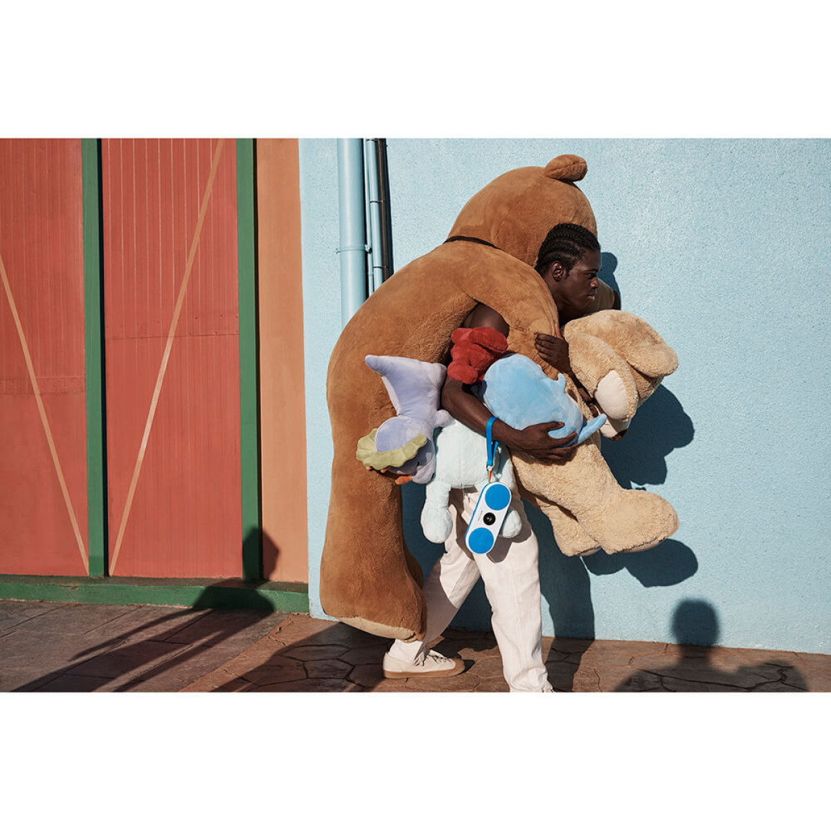 Osoba niesie dużego misia i pluszaki. W tle niebieska ściana i czerwone drzwi.