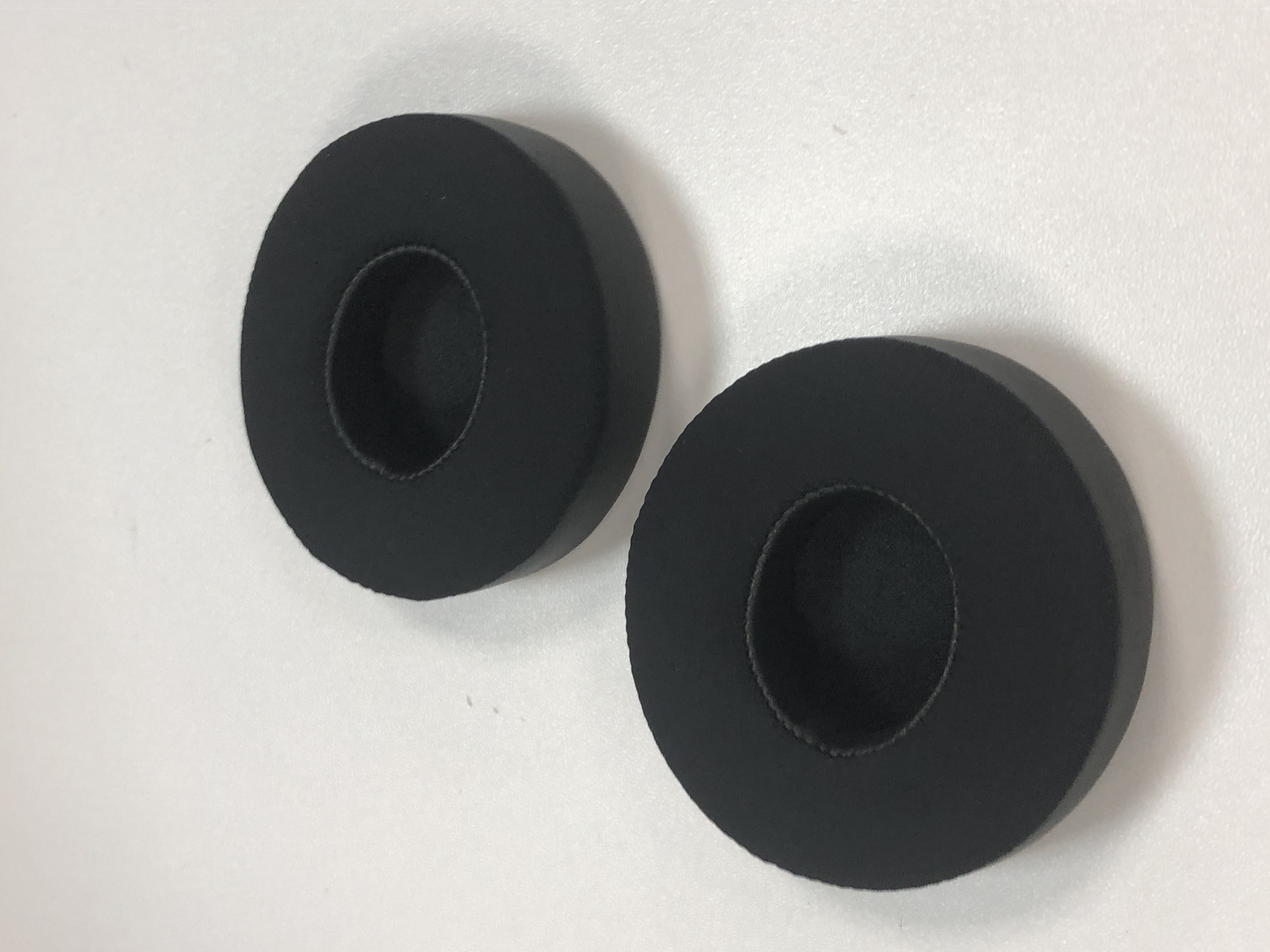Zwei schwarze, kreisförmige Ohrpolster. Sie liegen auf einer weißen Oberfläche. Die Pads haben ein Loch in der Mitte.