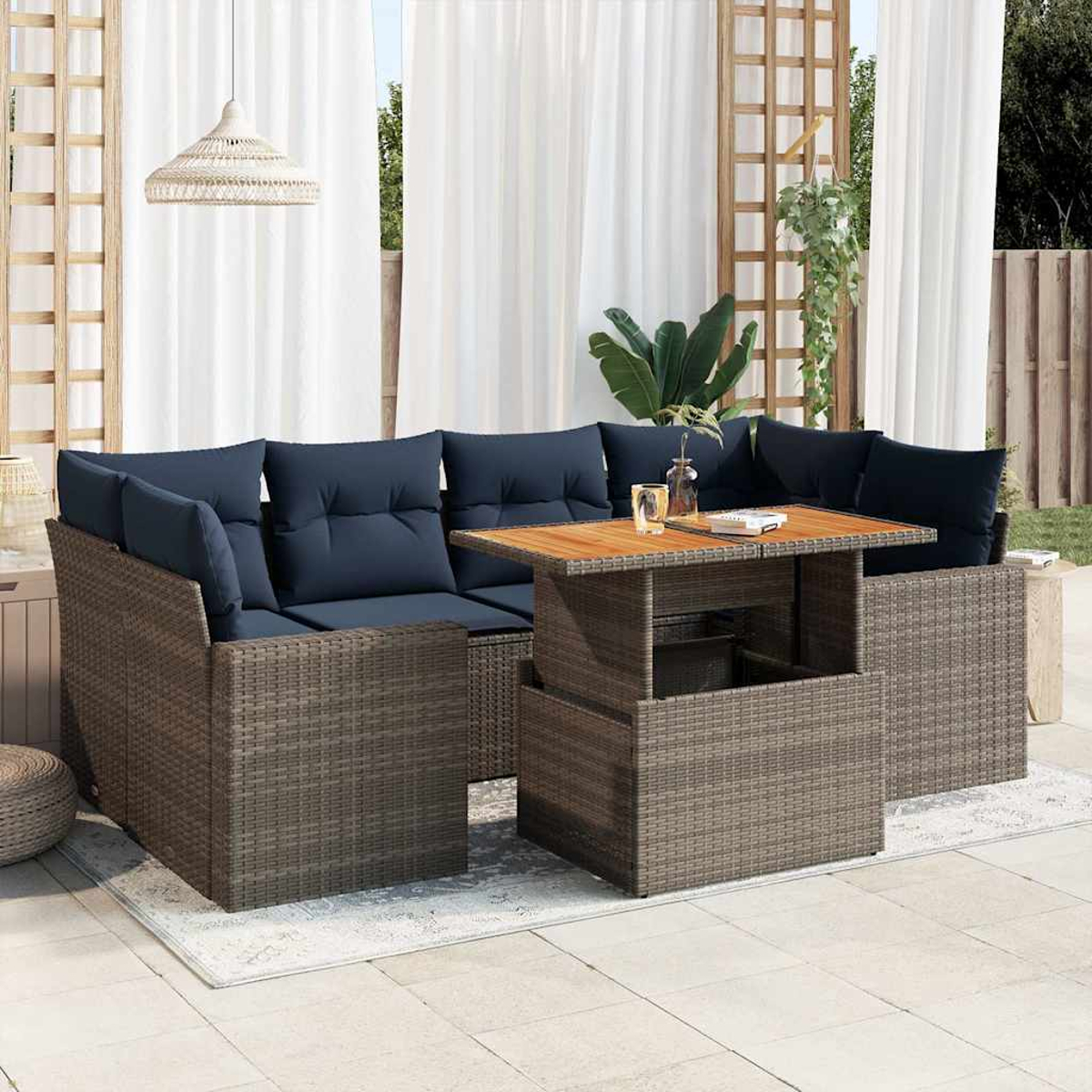 Gartenmöbel aus Korbgeflecht mit blauen Kissen, einem Tisch mit Hebefunktion und weißem Vorhanghintergrund.