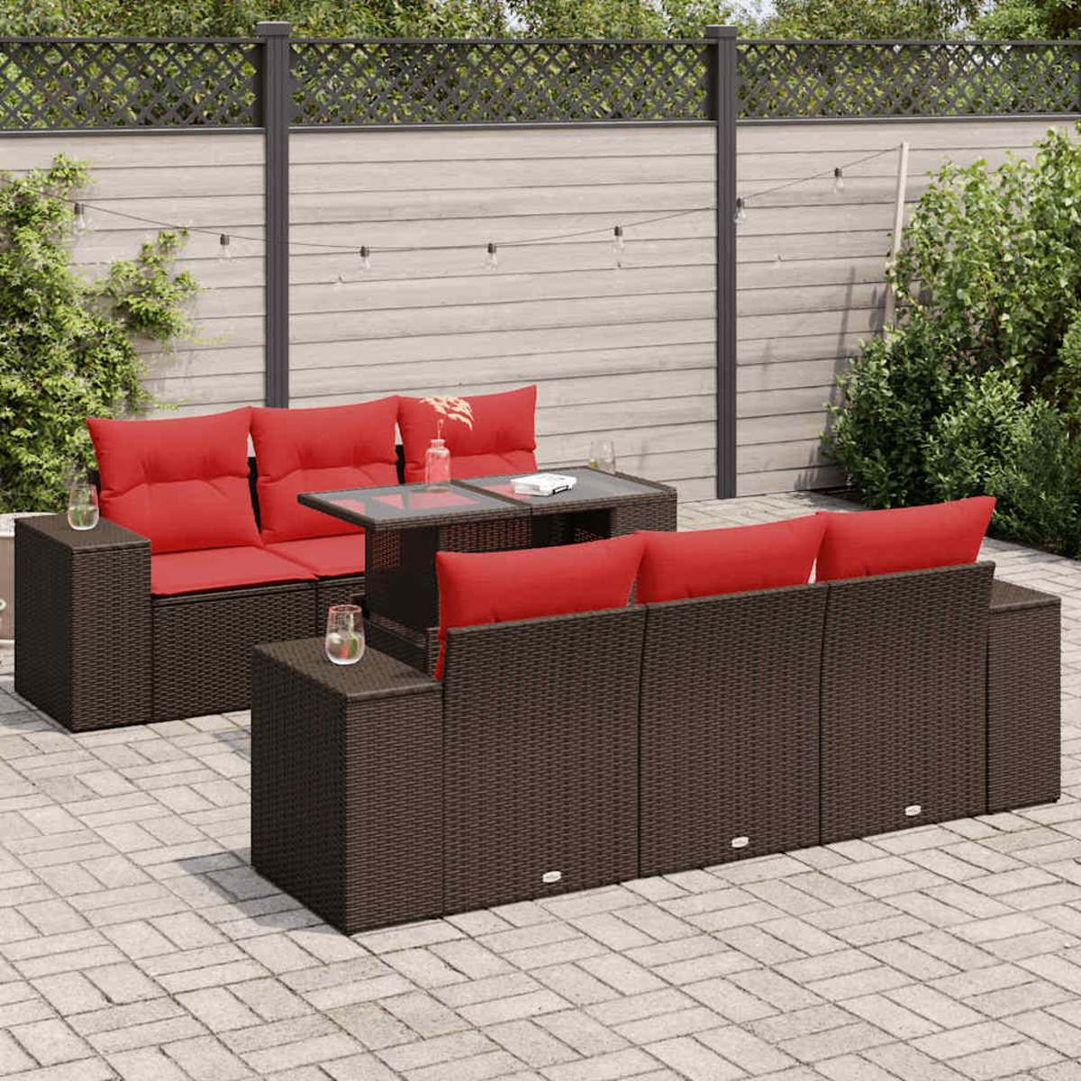 Ein Terrassenset mit braunen Rattanmöbeln, roten Kissen und einem Tisch mit Glasplatte. Die Szene ist tagsüber.