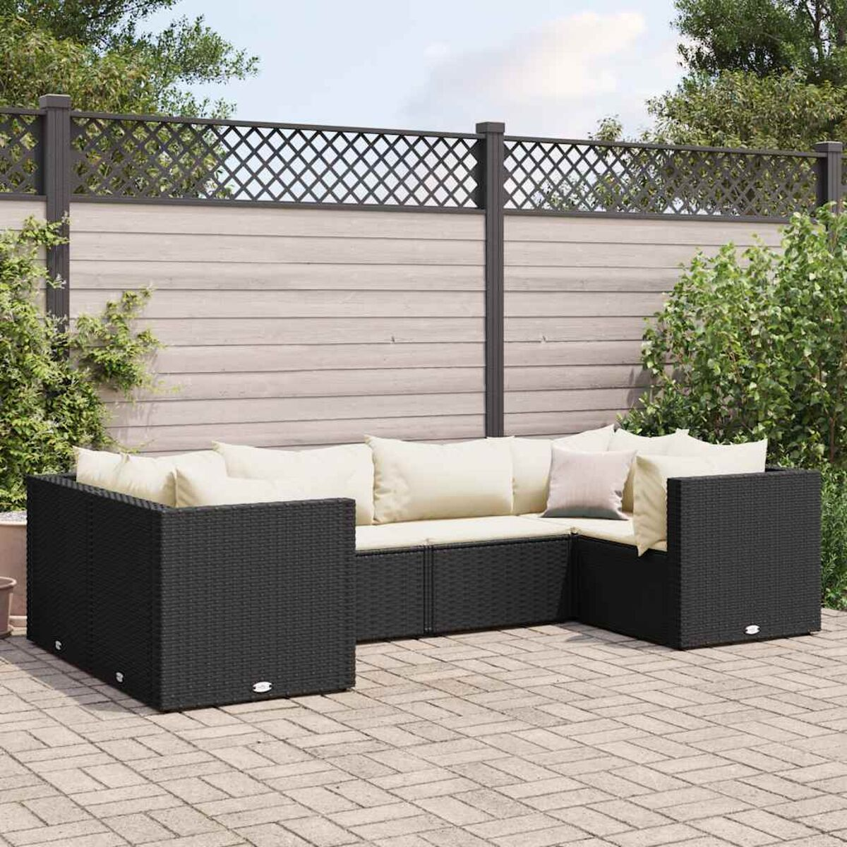 Set di mobili da esterno neri intrecciati con cuscini color crema. Patio in mattoni e recinzione in legno.