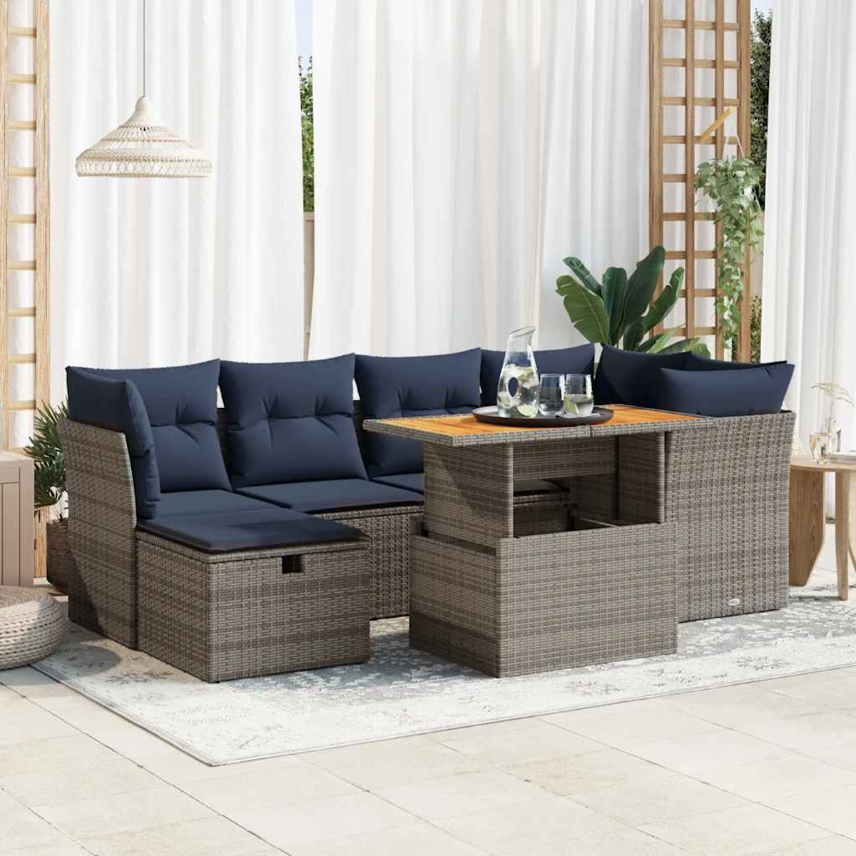 Rattan-Ecksofa mit blauen Kissen und einem Tisch. Die Szene spielt in einem Garten. Graue Farbe.