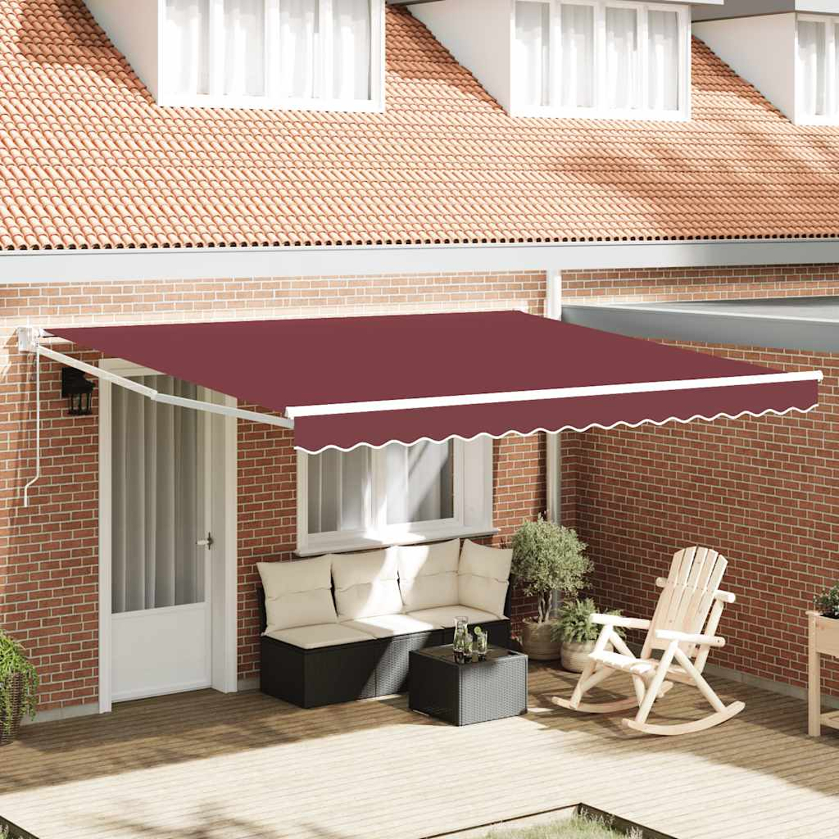 Eine weinrote Markise über einer Terrasse mit Möbeln. Eine Backsteinmauer bildet den Hintergrund. Ein Haus mit Dachgauben im Hintergrund.
