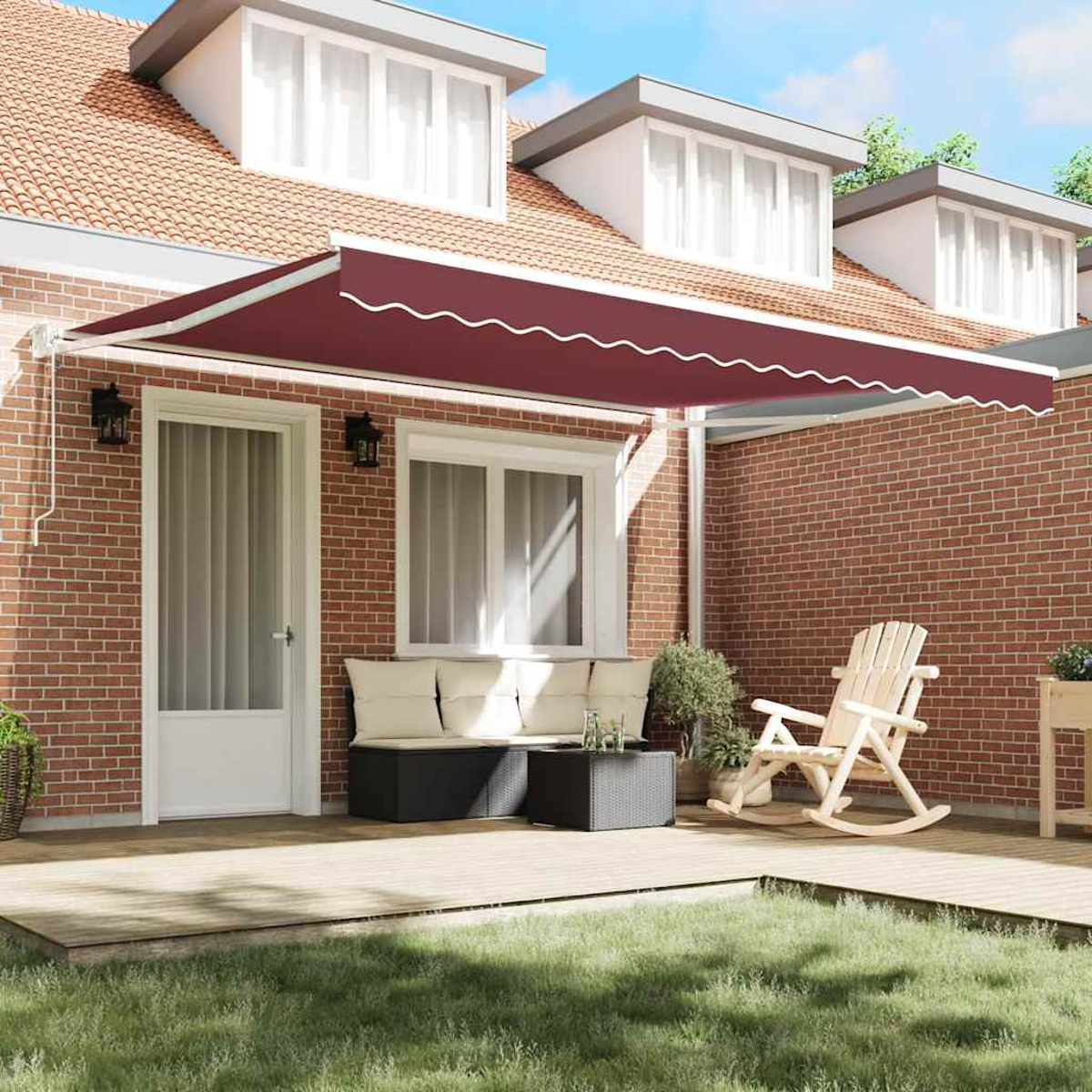 Eine weinrote Markise befindet sich über einer Terrasse mit Möbeln. Eine Backsteinmauer bildet den Hintergrund. Ein Haus mit Dachgauben im Hintergrund.