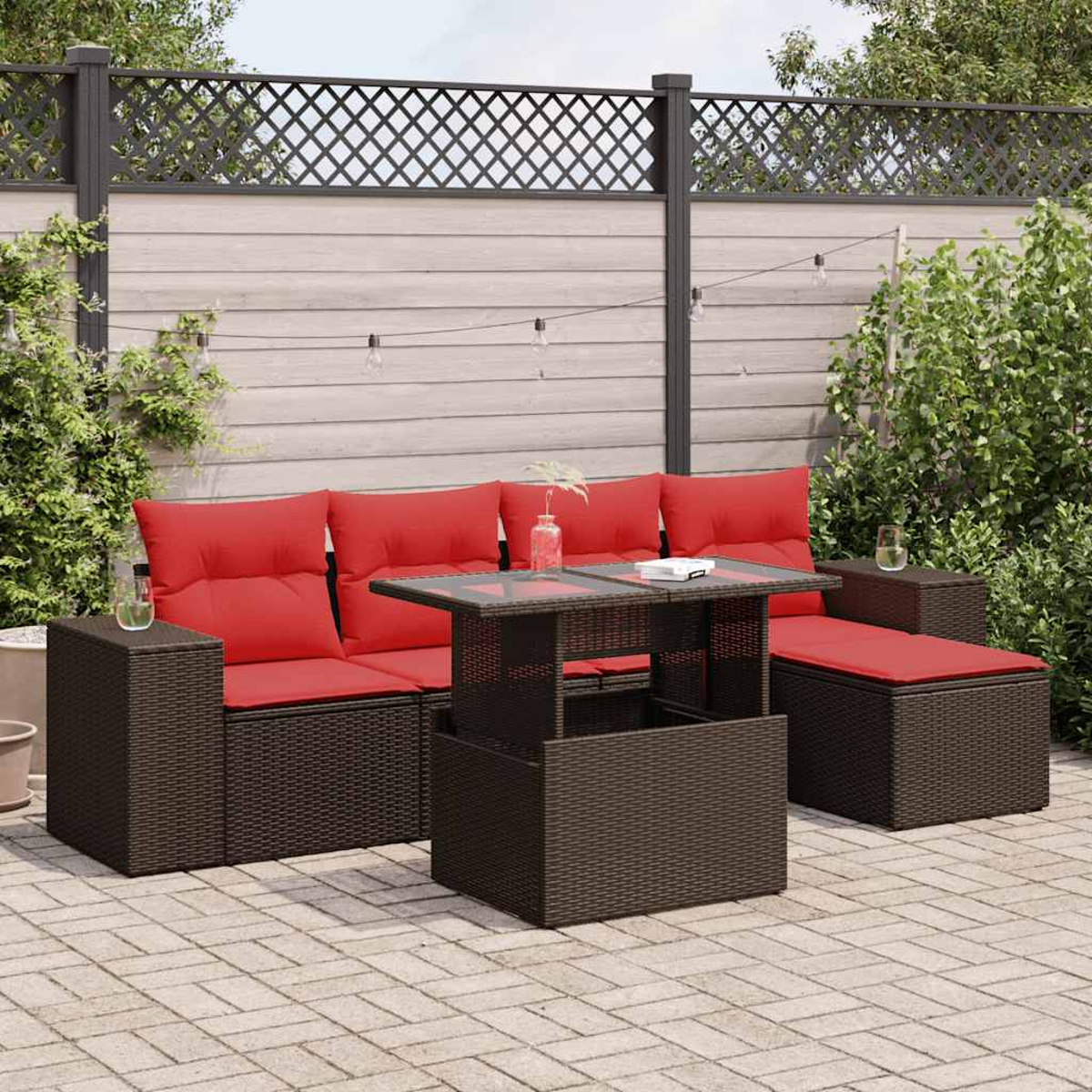 Terrassenset mit roten Kissen, Glastisch und Zaun im Hintergrund. Enthält Gläser und eine Vase.