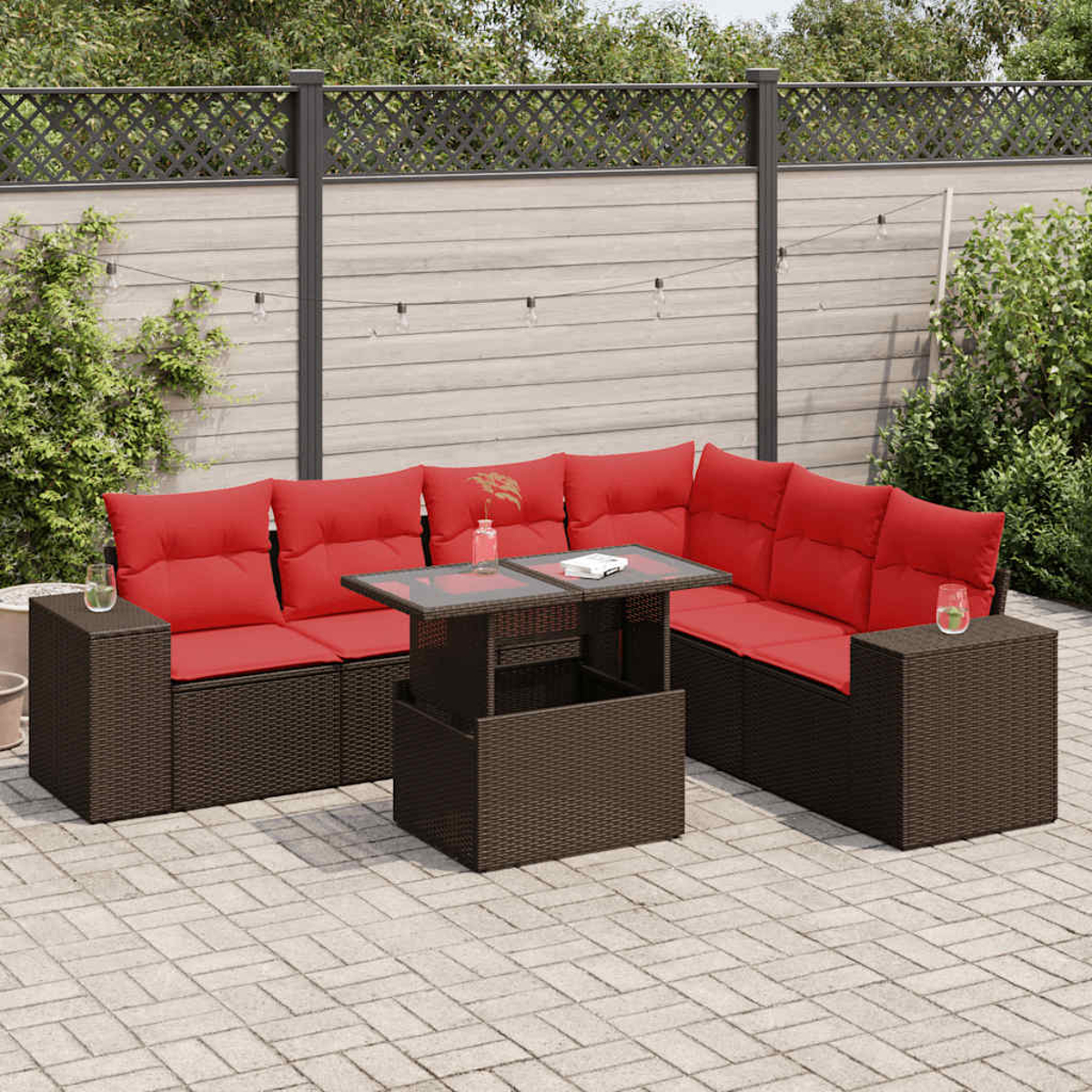 Ein braunes Ecksofa aus Korbgeflecht mit roten Kissen und einem Tisch mit Glasplatte auf einer Terrasse.