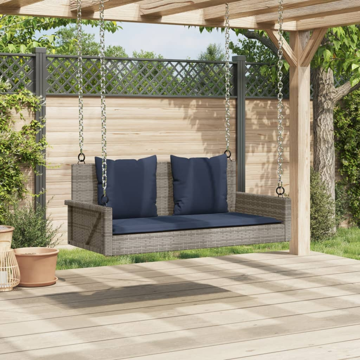 Altalena in rattan con cuscini blu in un giardino. Legno e piante verdi.