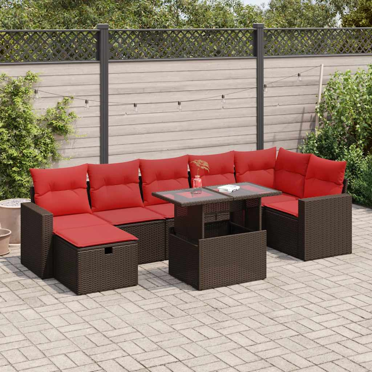 Gartensektionssofa mit roten Kissen und einem Tisch mit Glasplatte. Braunes Korbmöbel-Set auf einer Terrasse.
