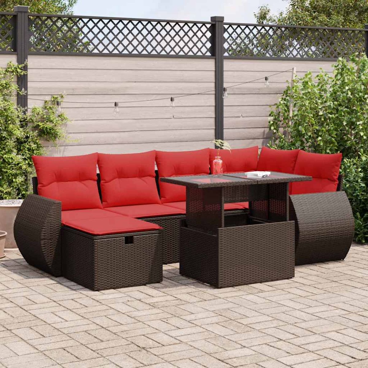 Ein dunkelbraunes Rattan-Ecksofa mit roten Kissen und einem Tisch mit Hubplatte auf einer Ziegelterrasse.