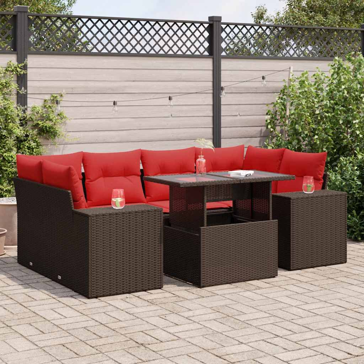 Outdoor-Sitzgruppe mit braunem Korbmöbelsofa, roten Kissen und einem Tisch mit Hubfunktion.