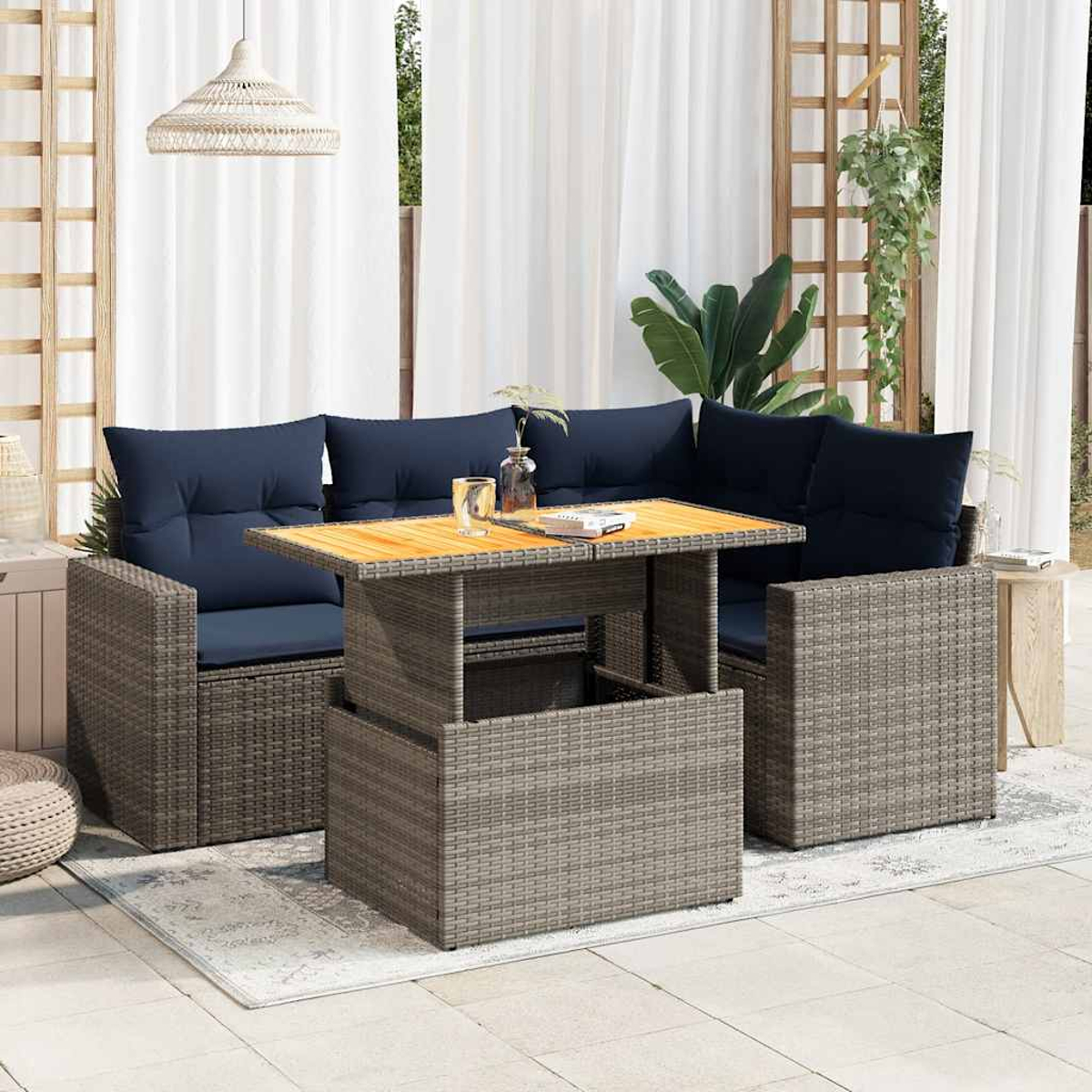 Outdoor-Sitzgruppe aus Korbgeflecht mit blauen Kissen und einem Tisch mit Hubfunktion. Pflanzen, Vorhänge und eine Lampe sind ebenfalls sichtbar.
