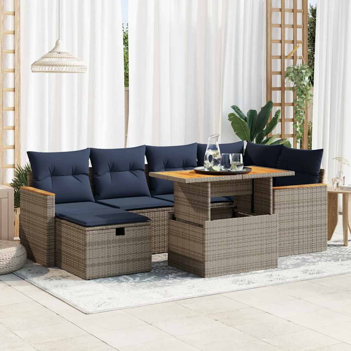 Outdoor-Ecksofa mit hochklappbarem Tisch. Blaue Kissen, Rattangestell und weiße Vorhänge.