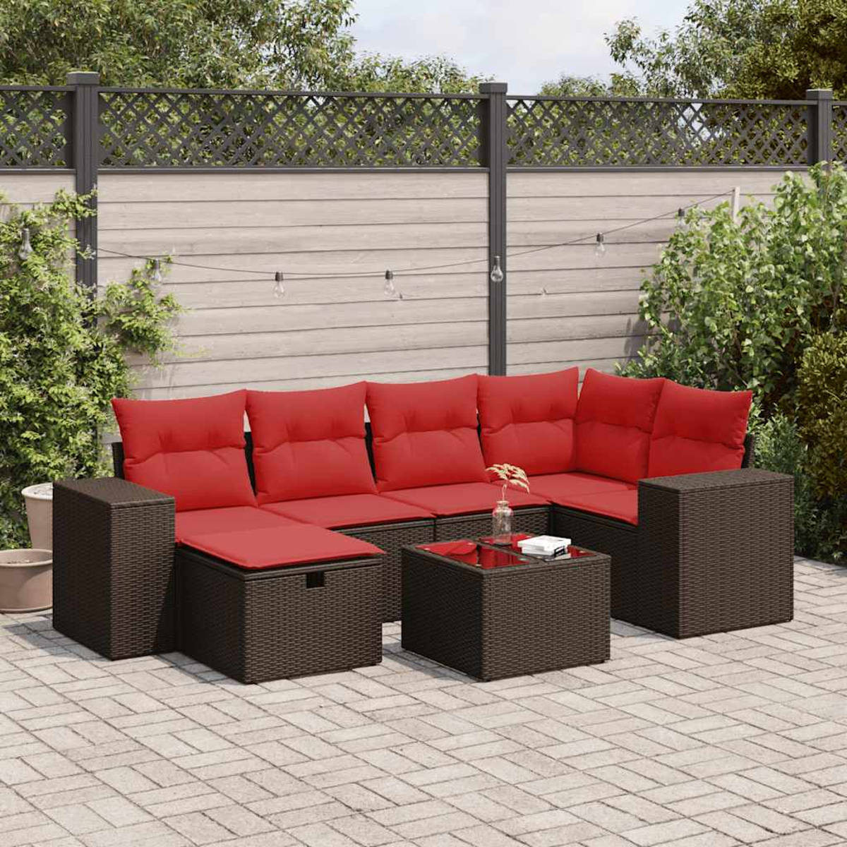 Ein braunes Rattan-Sofaset mit roten Kissen auf einer Ziegelterrasse. Ein Glastisch davor.