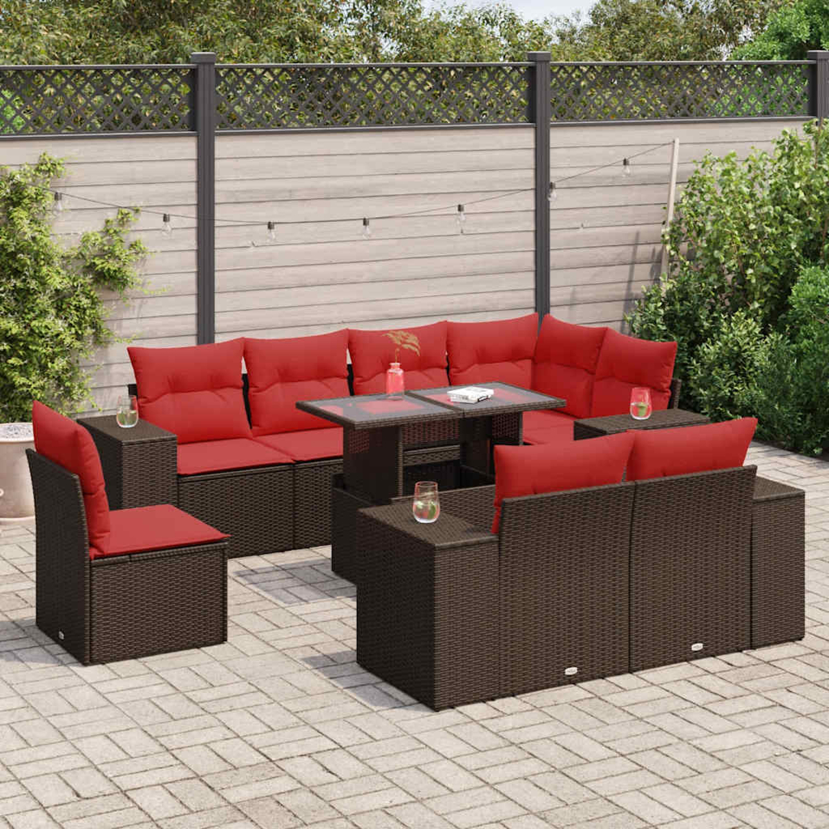 Outdoor-Ecksofa mit braunem Korbgeflecht, roten Kissen und Tischen. Auf einer Backsteinterrasse mit Pflanzen.