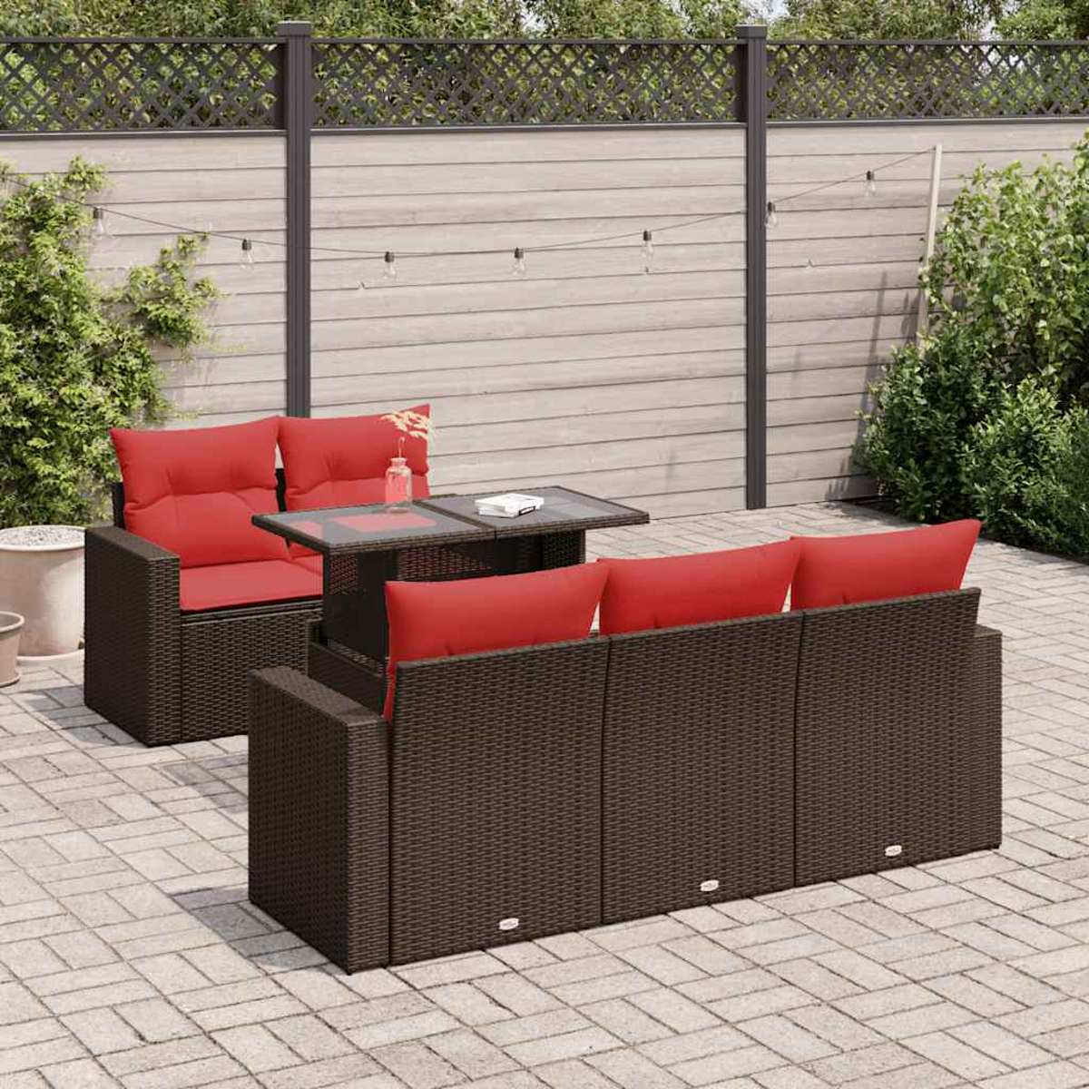 Braunes Outdoor-Wicker-Sofaset mit roten Kissen und einem Tisch mit Glasplatte. Hinterhof mit Holzzaun.